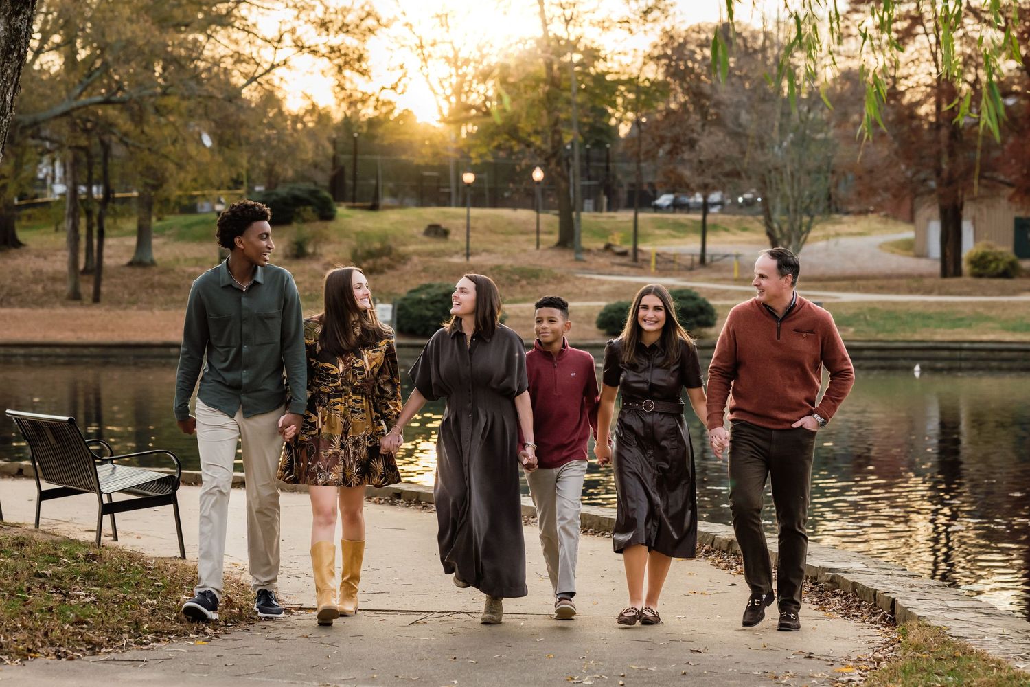 A group of young people walking together along a lakeside path at sunset in a park.