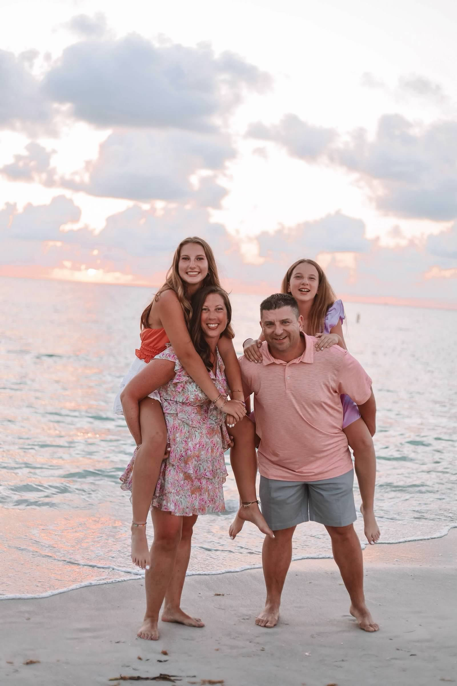 Family enjoying playful moments together on a sandy beach during golden hour.