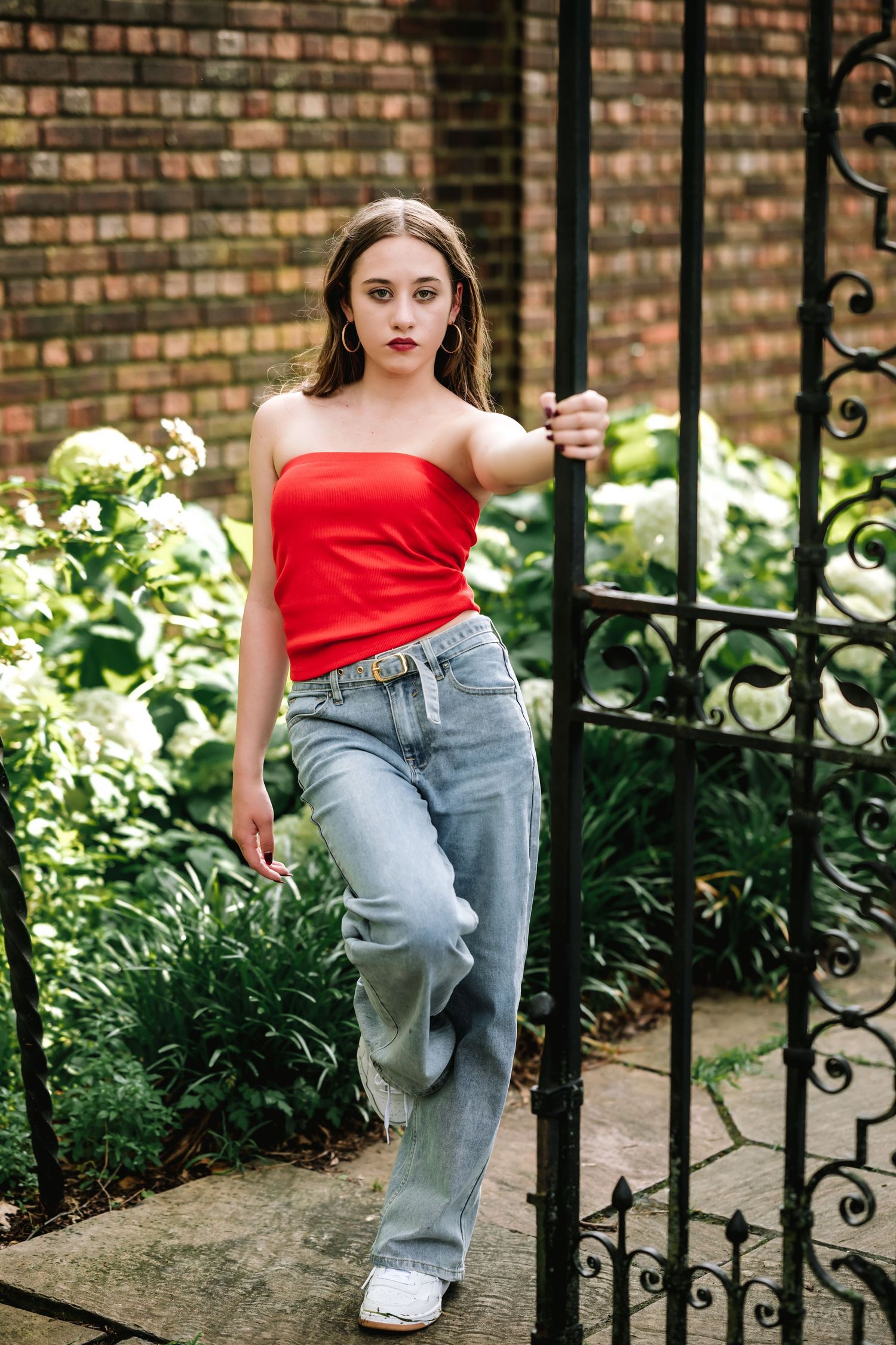 Person in red top and jeans poses playfully between ornate iron garden gates.