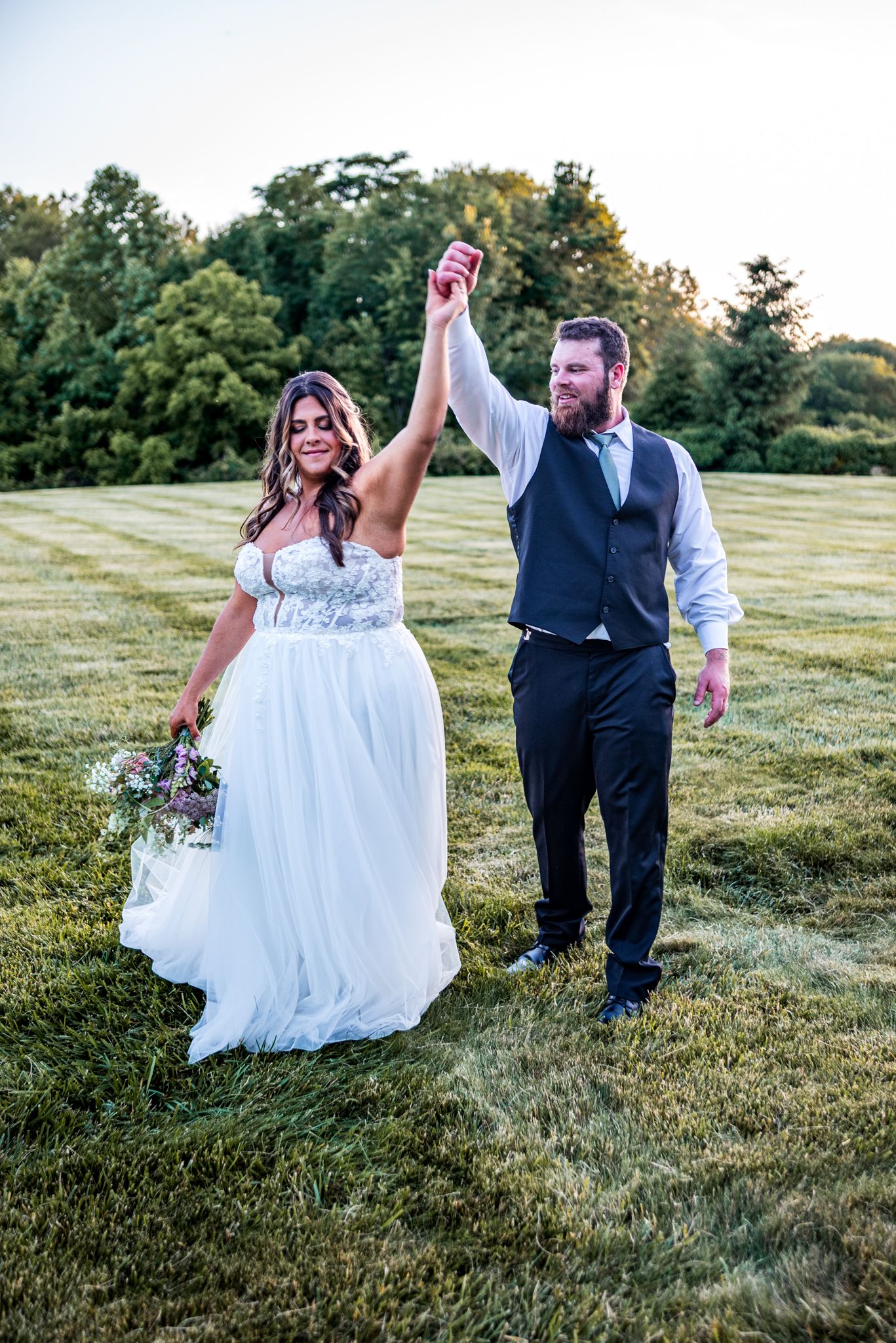 A couple dances joyfully on a grassy hillside during sunset, their silhouettes casting long shadows across the field.
