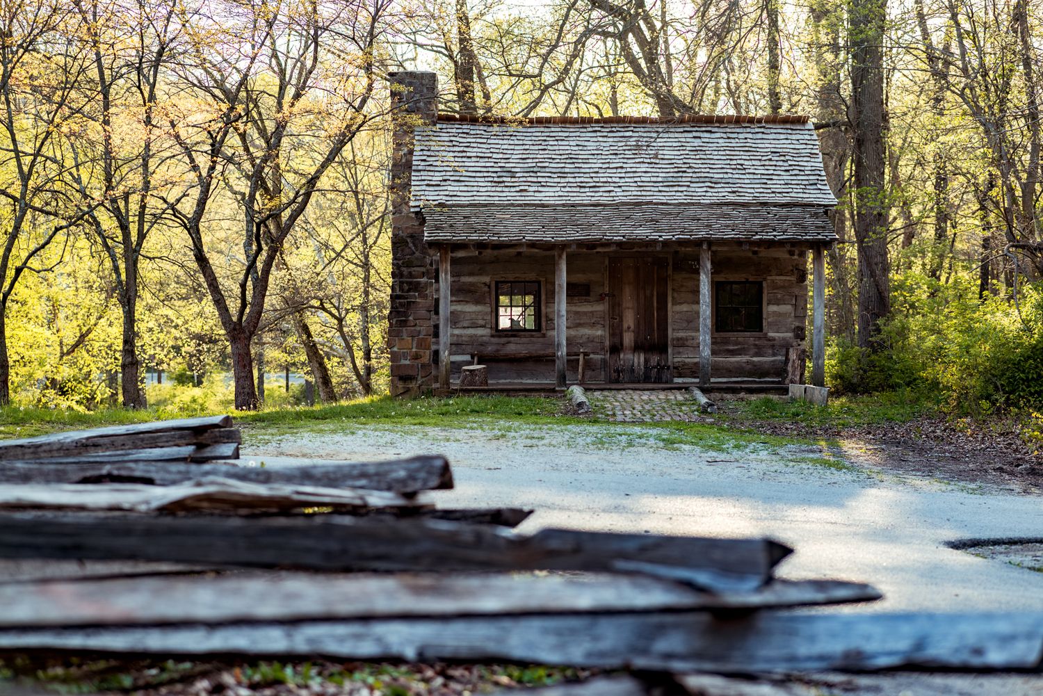 Rustic log cabin with stone foundation nestled in autumn woods along a country road.