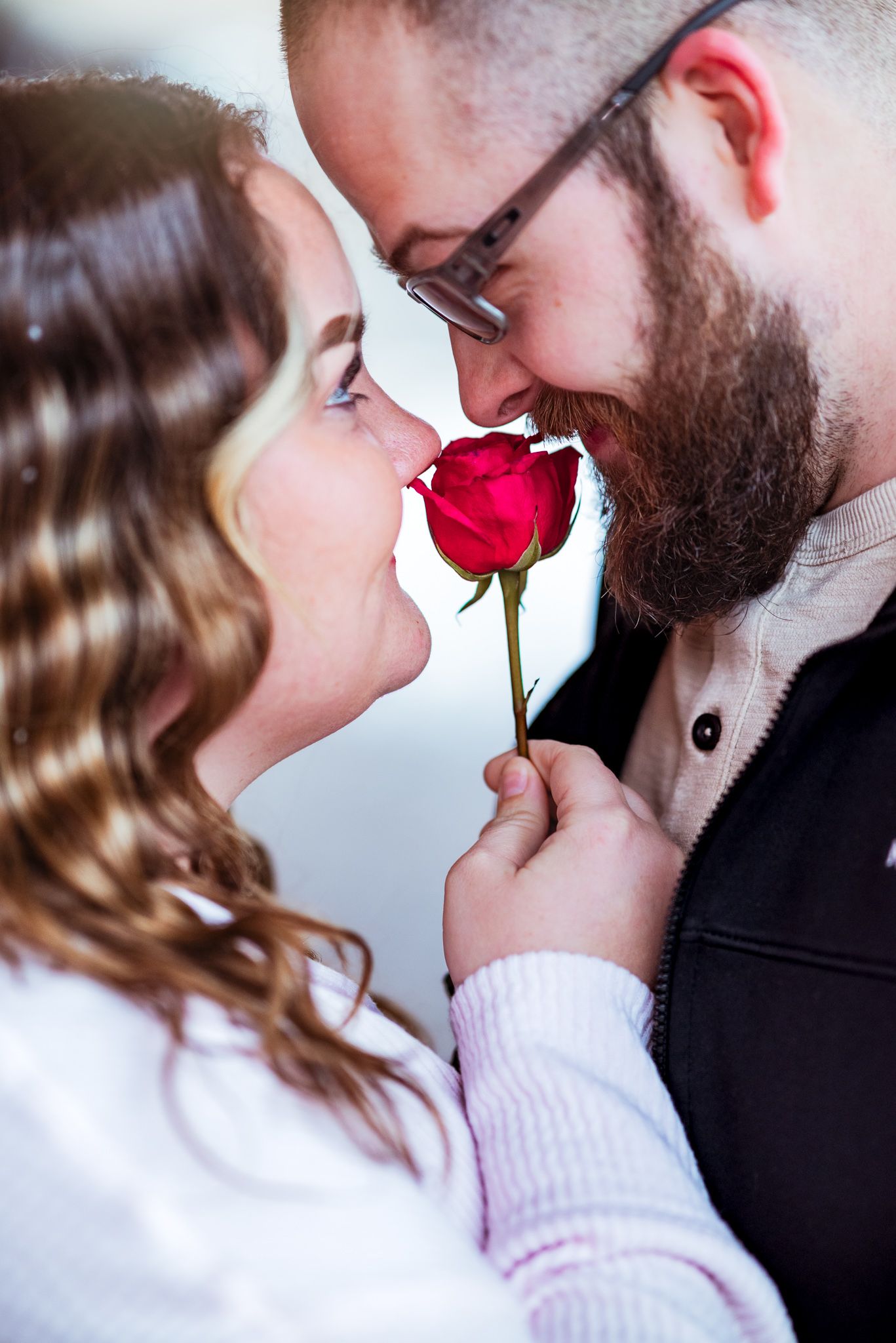 A couple shares a romantic moment with a red rose between them while posing for a close-up photo.