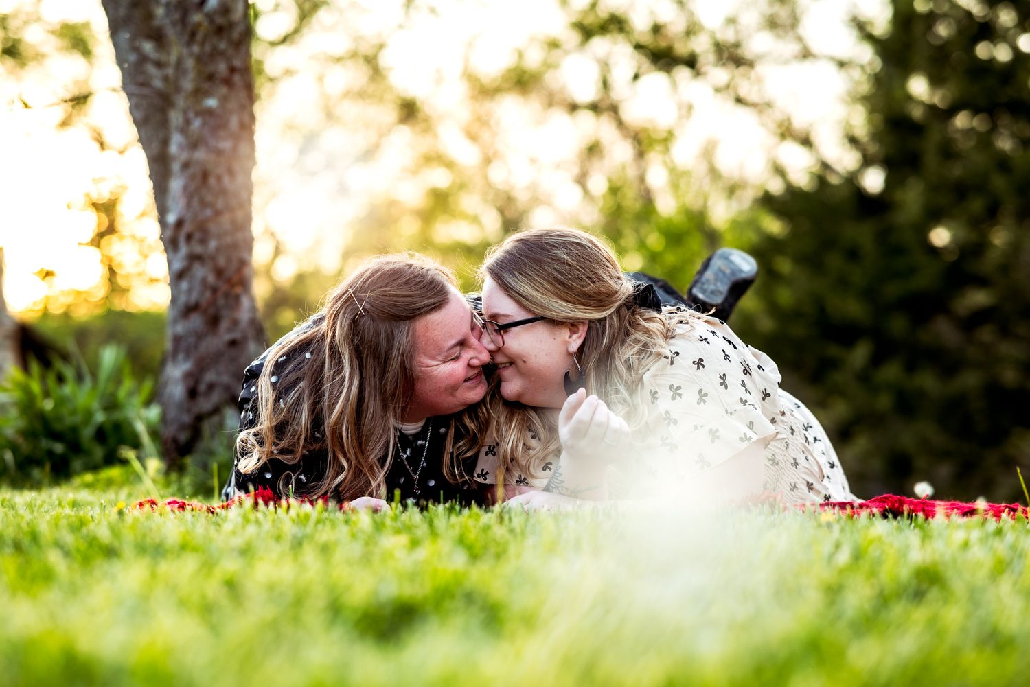 Two people laying on grass during golden hour sharing an intimate moment together.