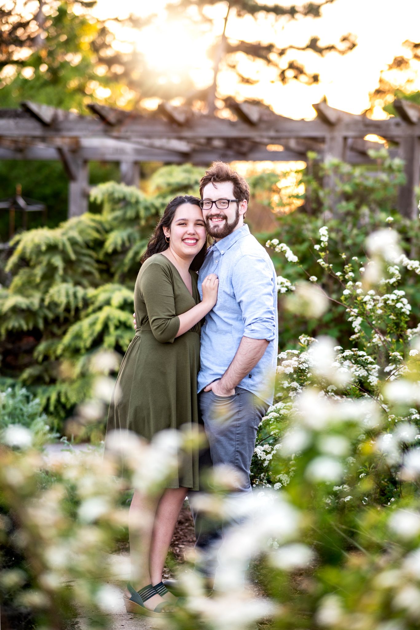 A couple shares intimate moments among blooming white wildflowers in a garden setting during golden hour.