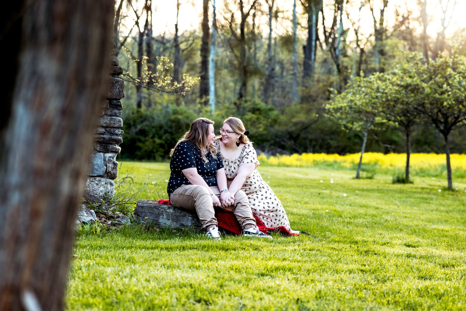 A couple sits together on lush grass during golden hour in a spring garden setting.