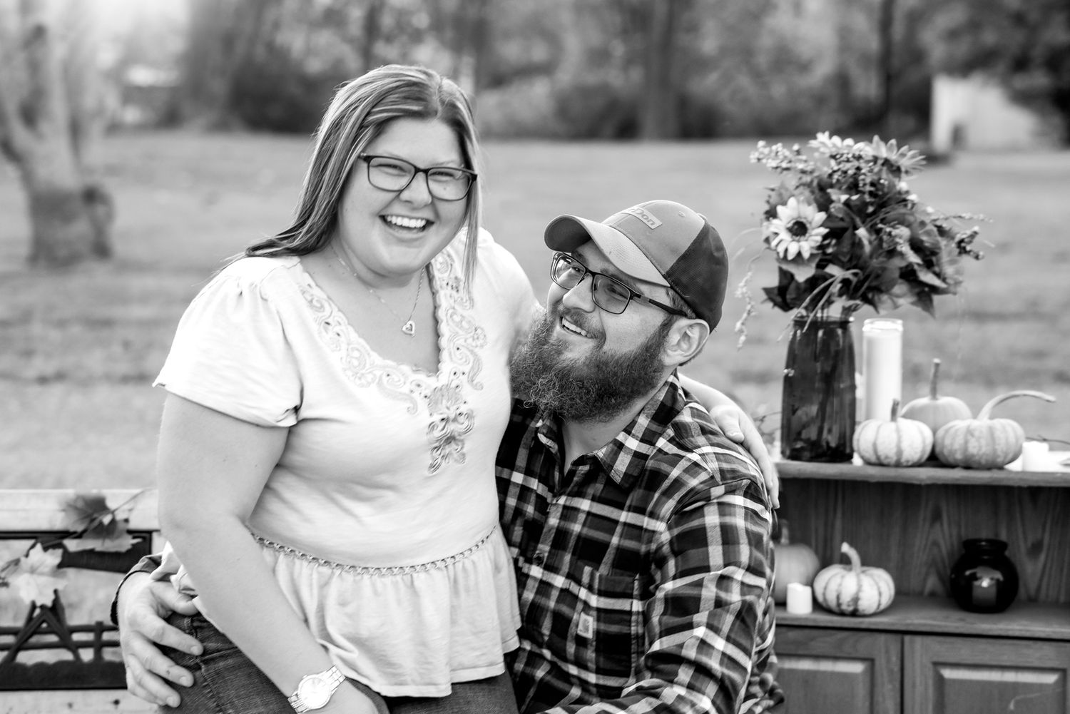 A black and white portrait in an outdoor autumn setting with pumpkins and flowers.