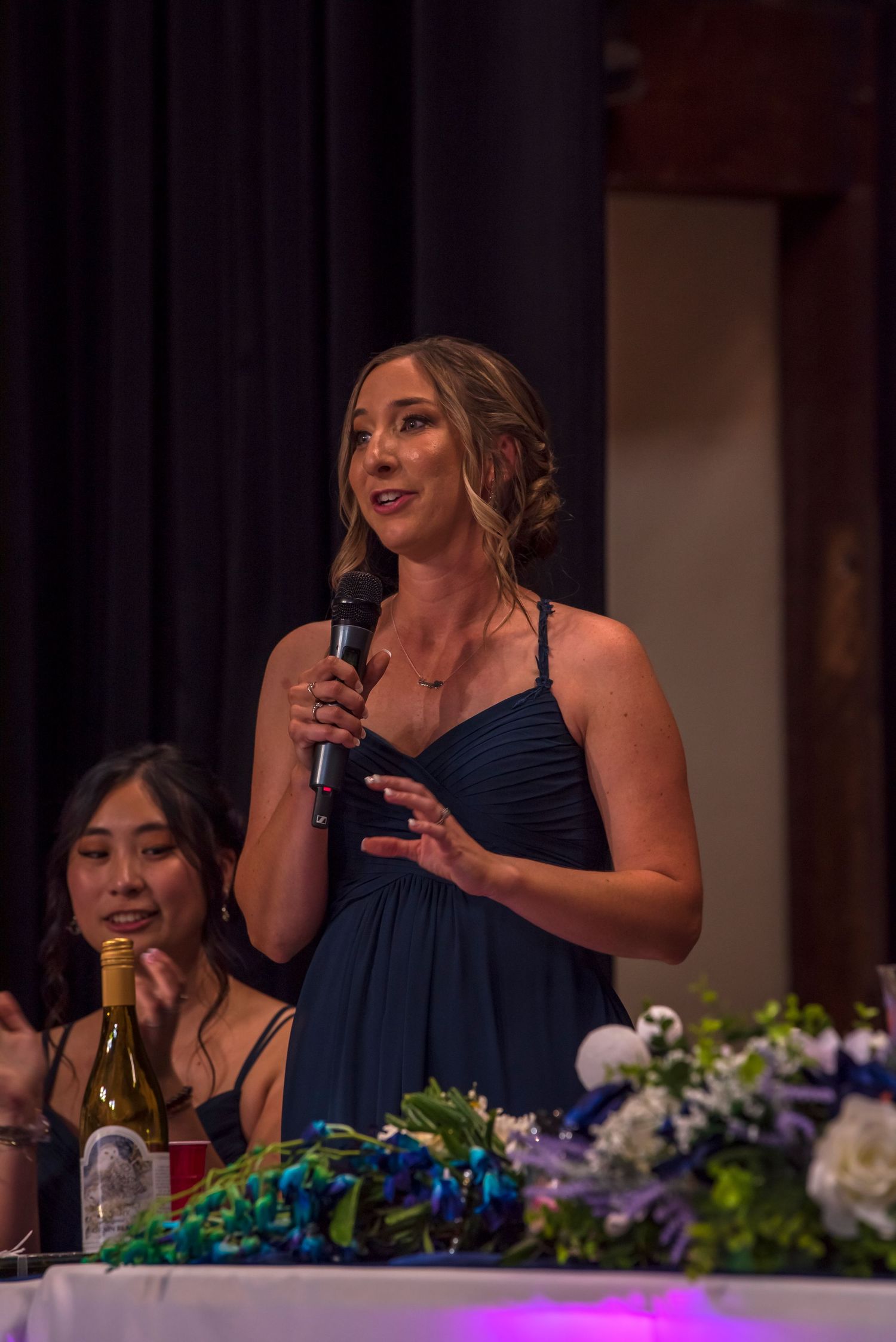 Wedding reception speech given at decorated head table with floral arrangements.