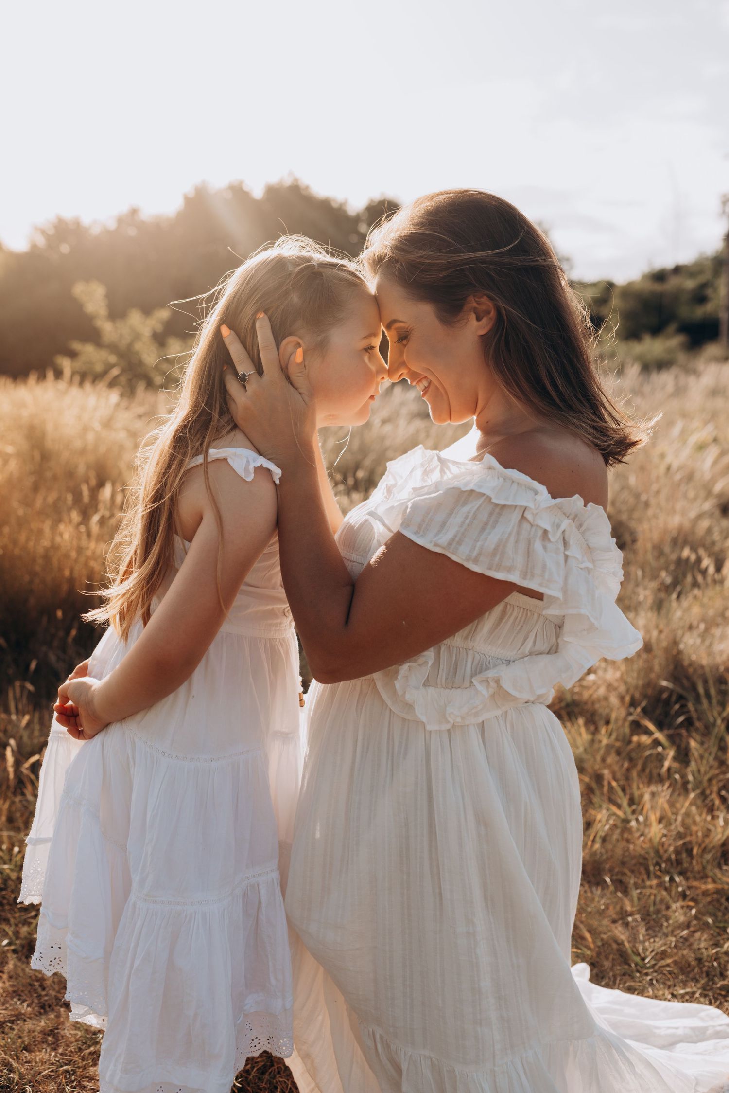 Two people in white dresses share an intimate moment in a golden field at sunset.