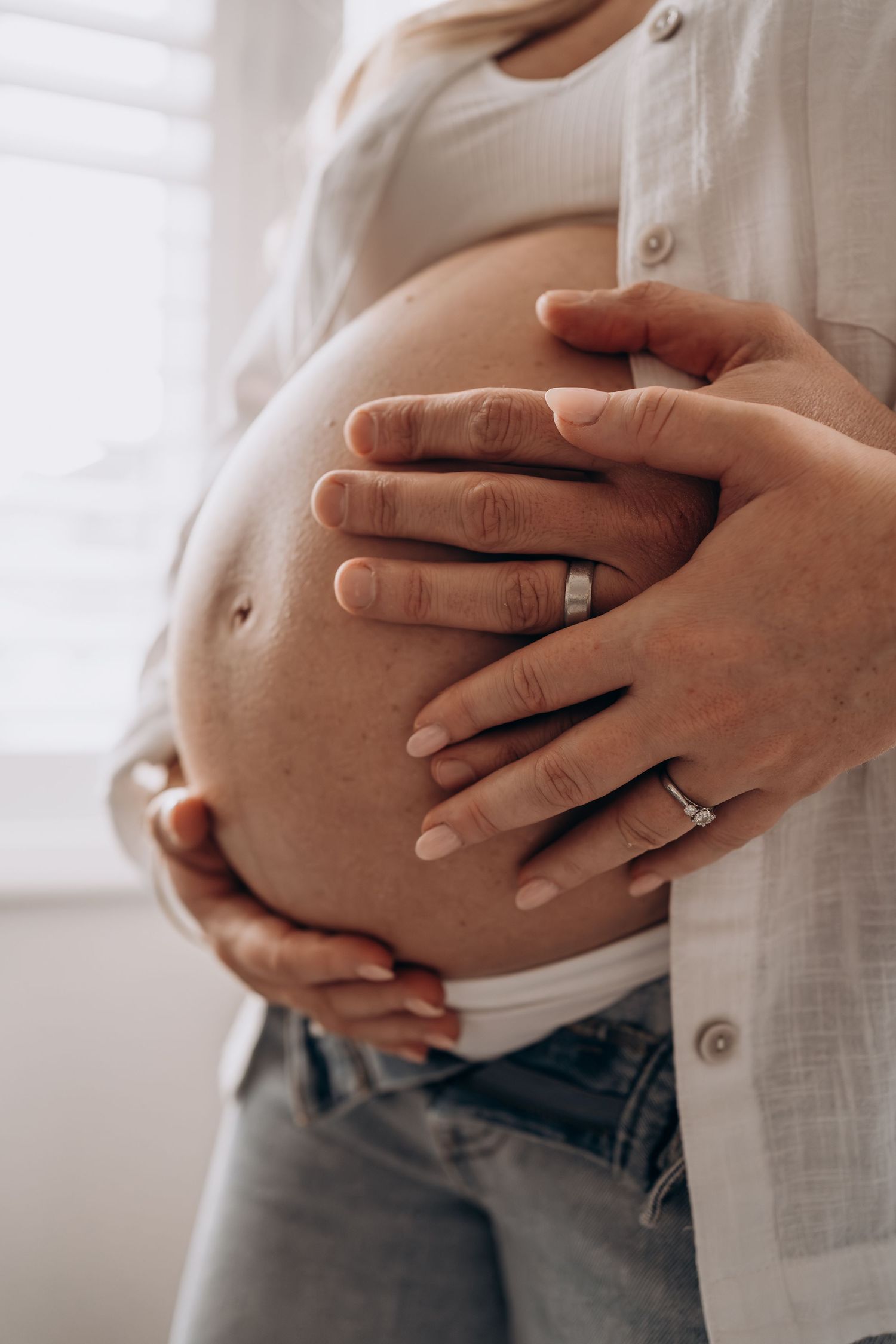 Close-up series of hands cradling a pregnant belly while wearing a white button-down shirt and jeans.