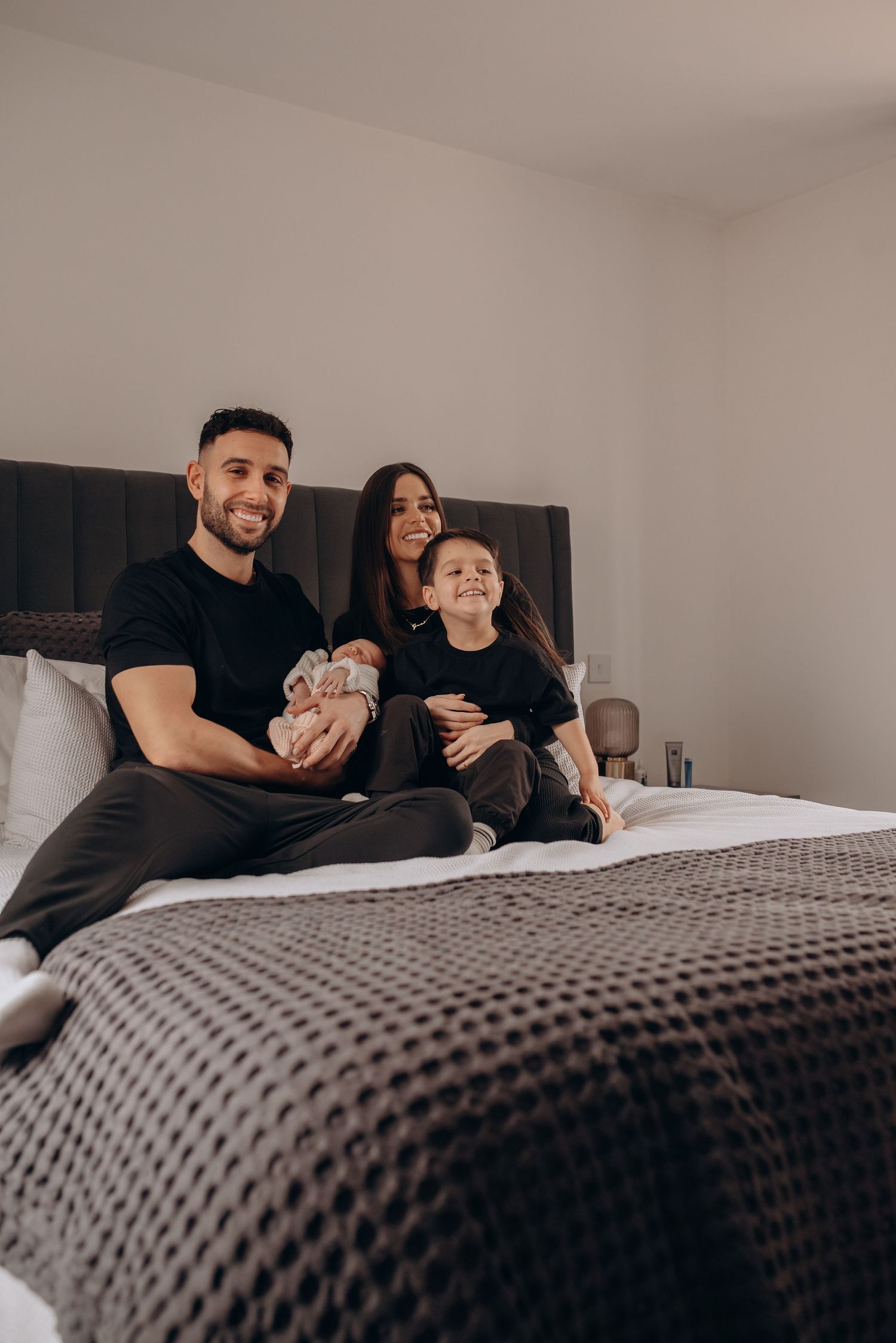 Family relaxing together on a gray bedspread in a bright bedroom.