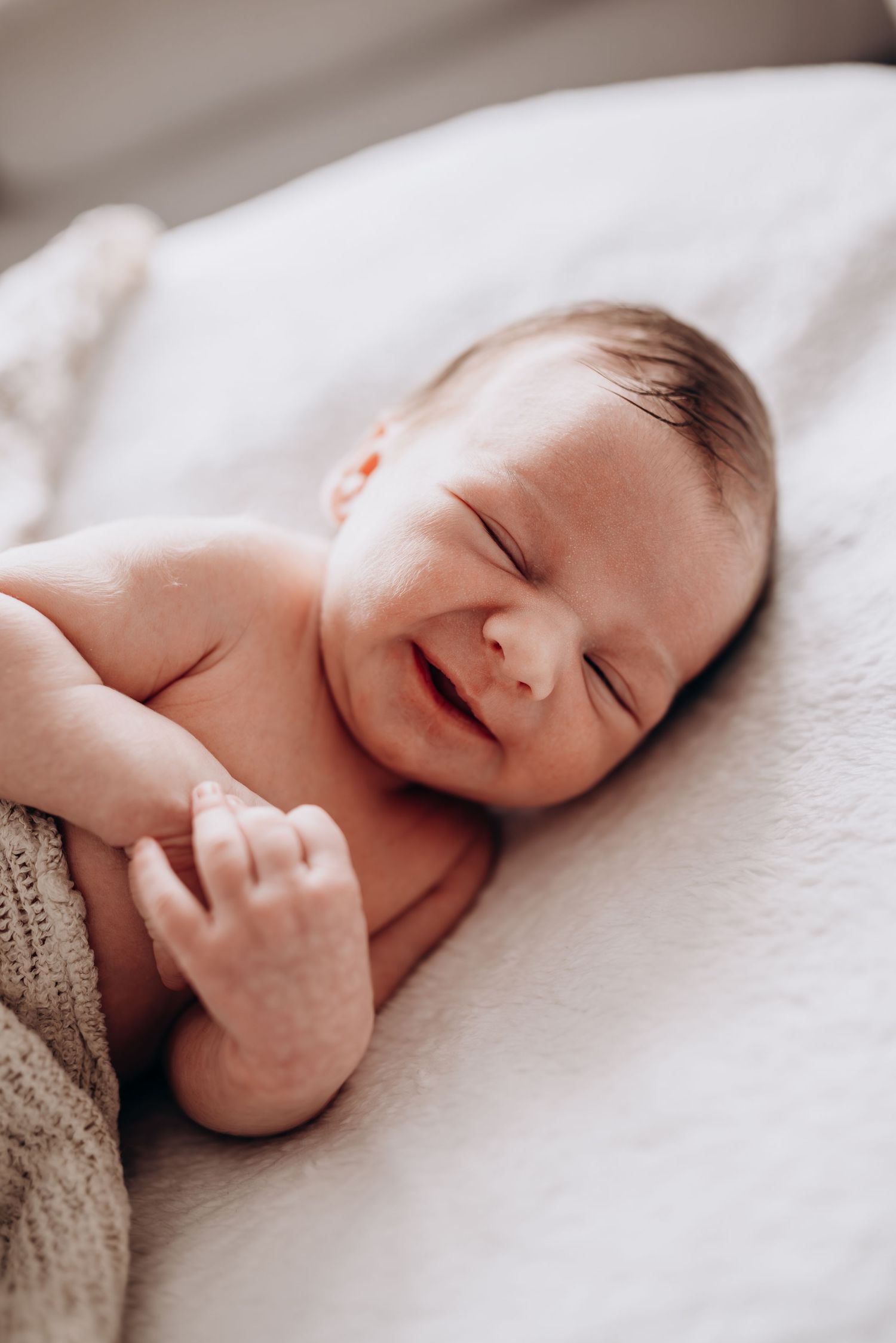 Peaceful newborn baby sleeping on white bedding in soft natural light.