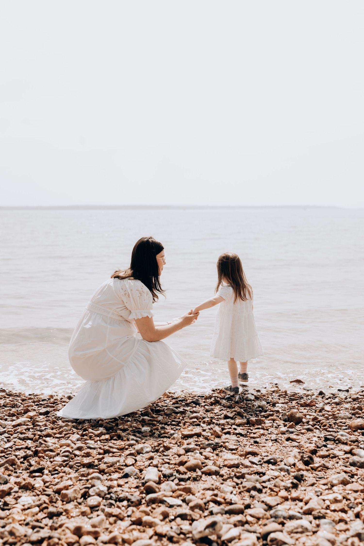 Mother and daughter share tender moment while sitting on rocky beach shore.