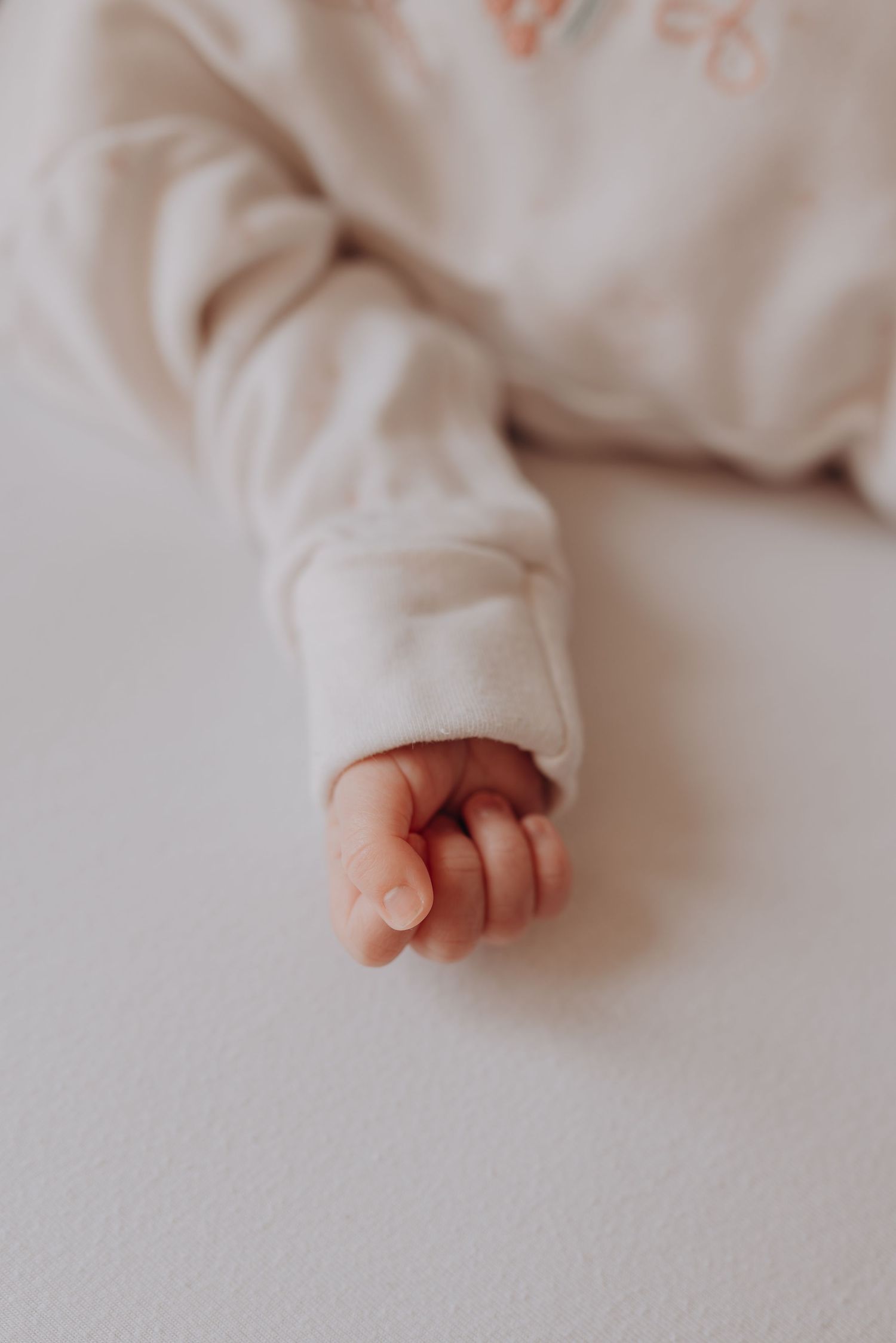 Close-up of baby's tiny hand against soft white fabric background.