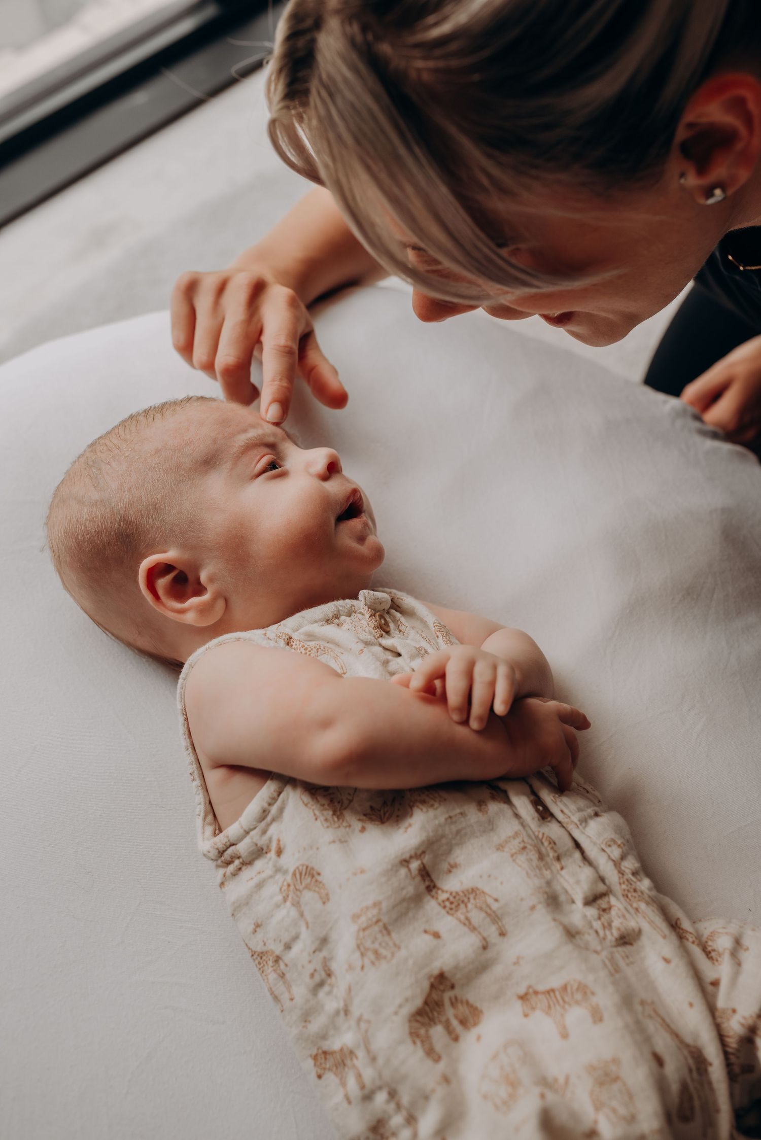 Baby laughing during playful interaction on white surface in natural light.