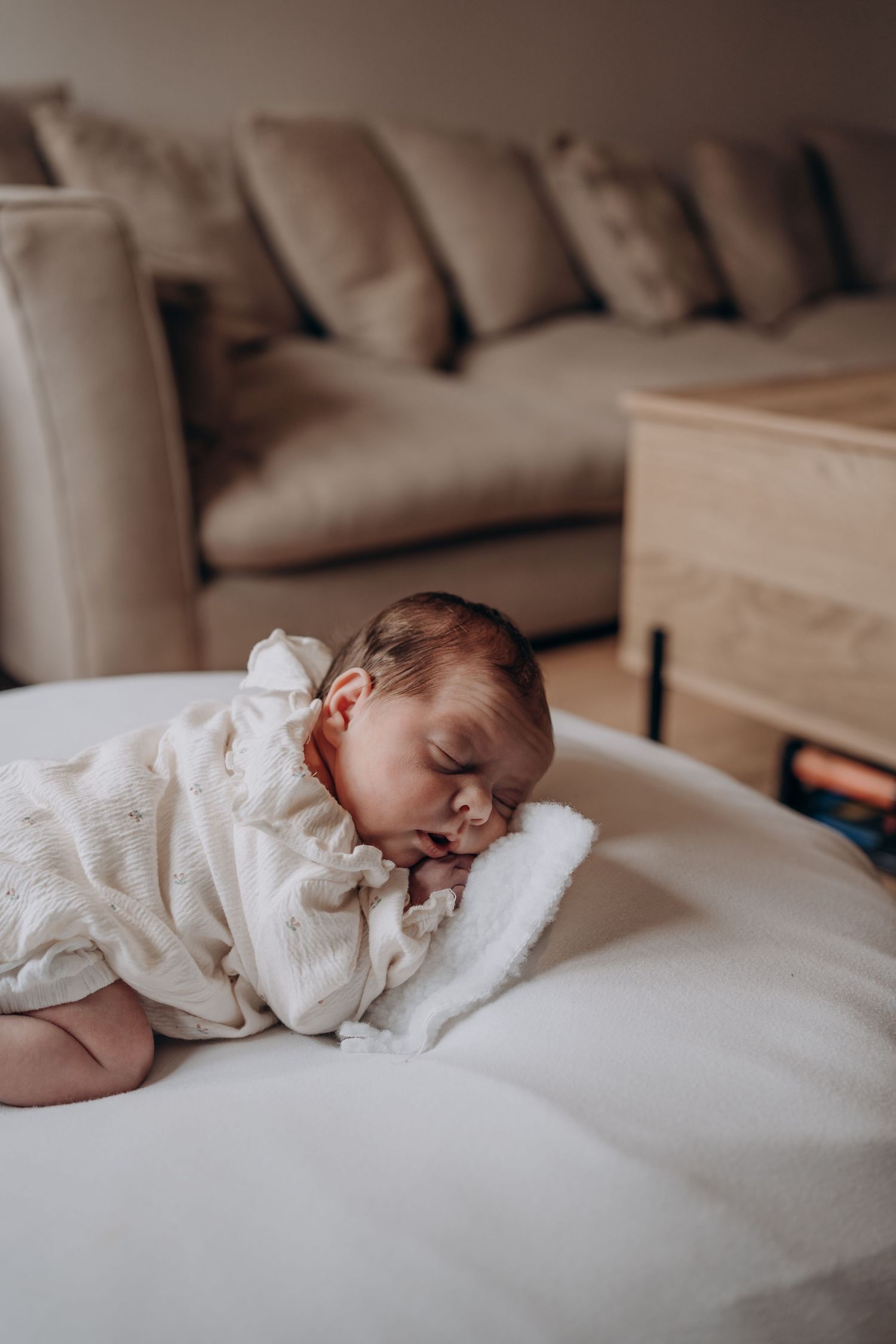 Peaceful newborn baby sleeping on a white fluffy surface, wrapped in a soft cream muslin cloth in a cozy living room.