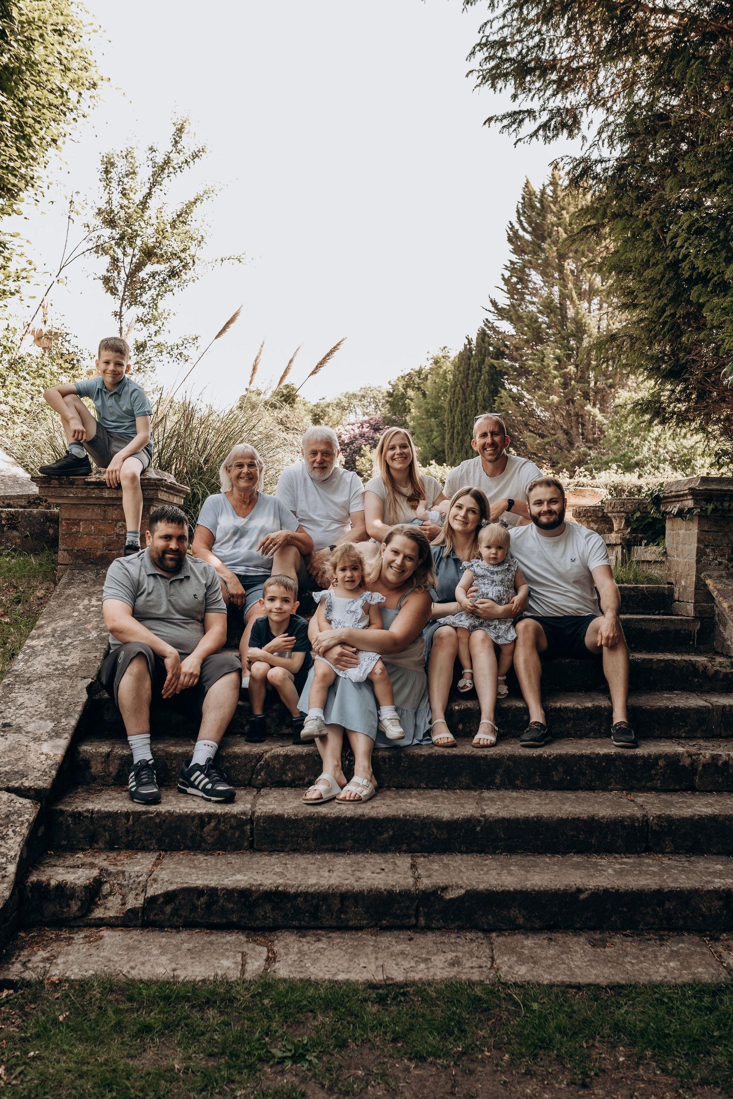 Large family group sits together on outdoor stone steps for casual portrait.