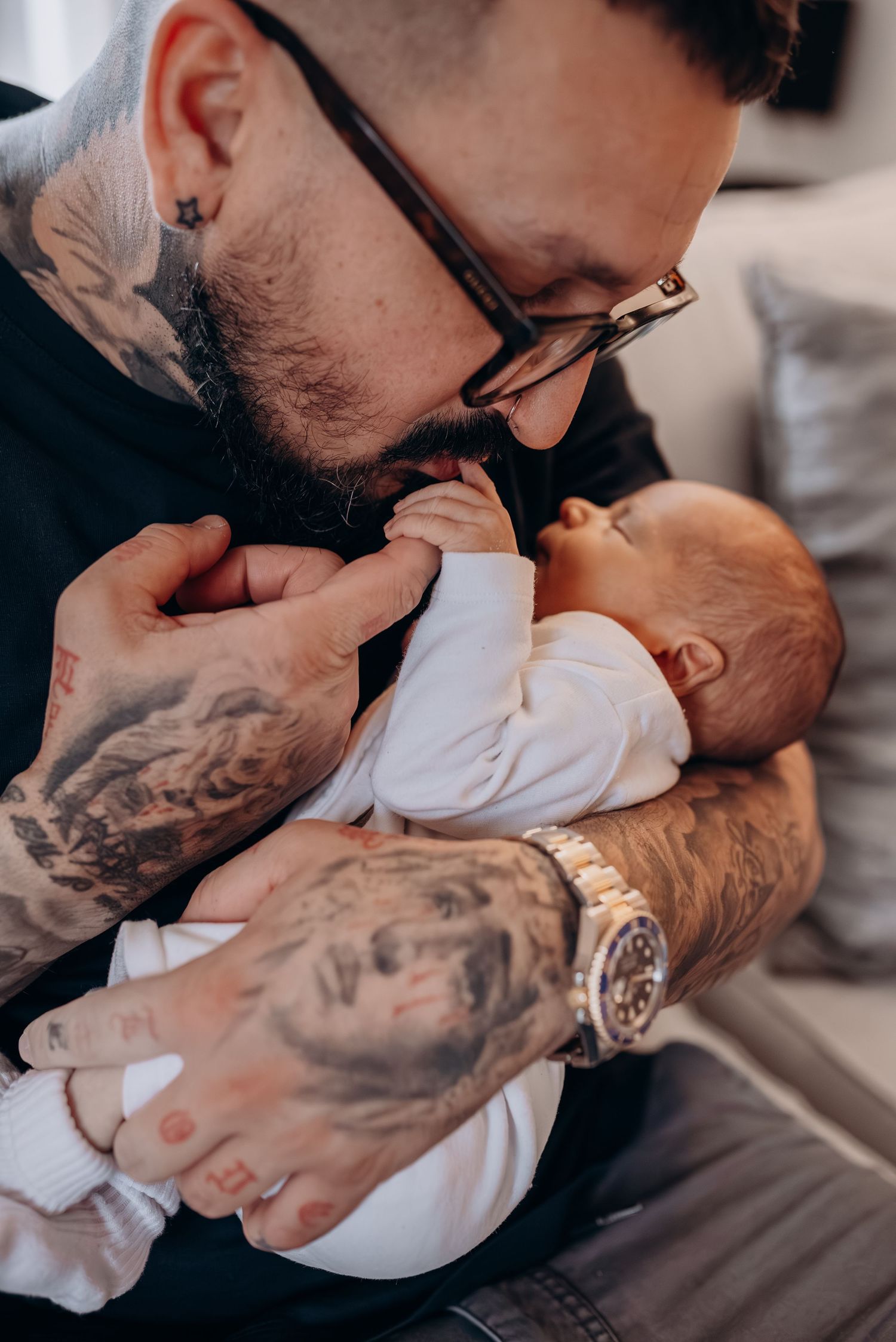 Close-up shots of tattooed arms holding and cradling a newborn baby in white clothing.