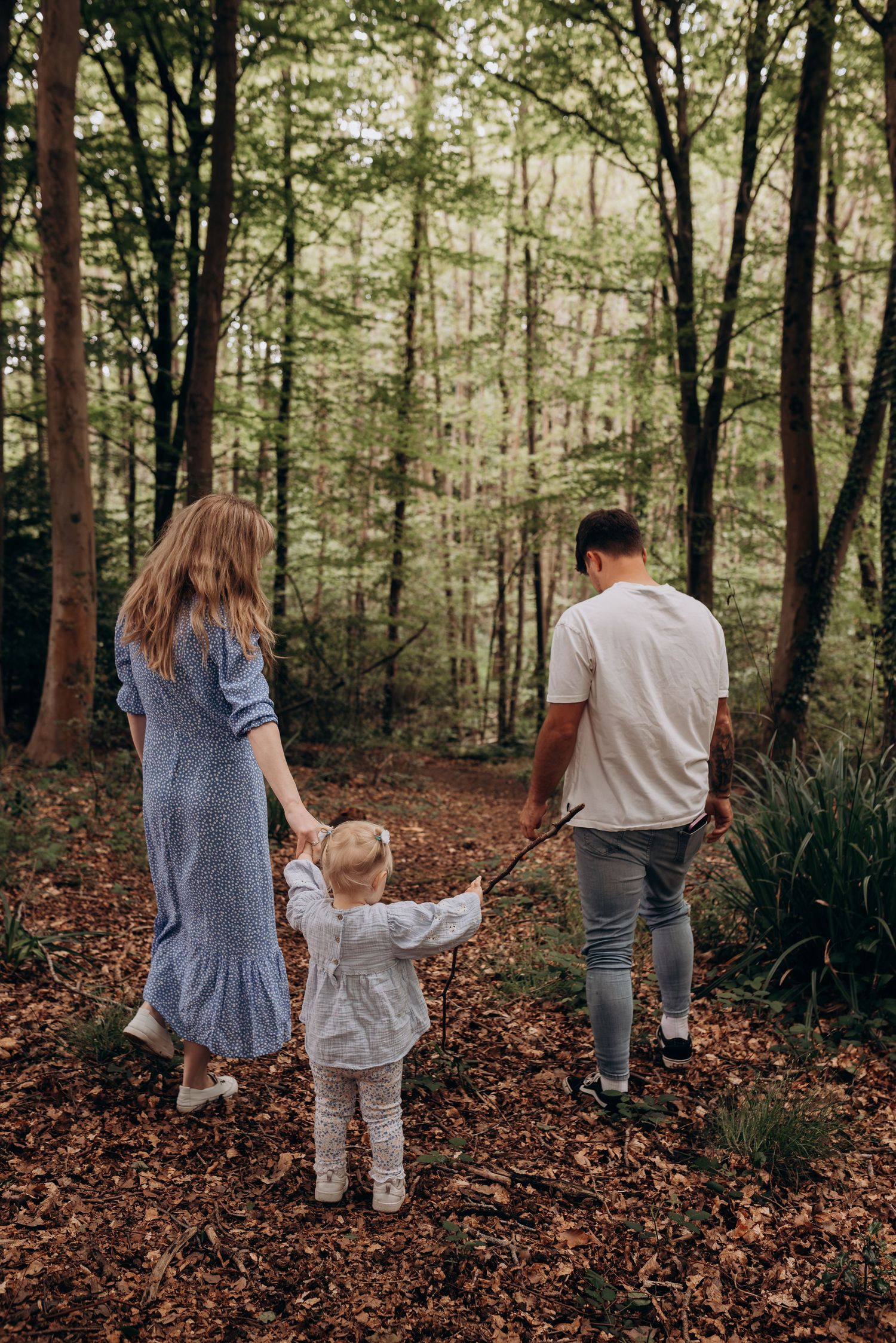 Family walking through autumn forest with fallen leaves on ground.