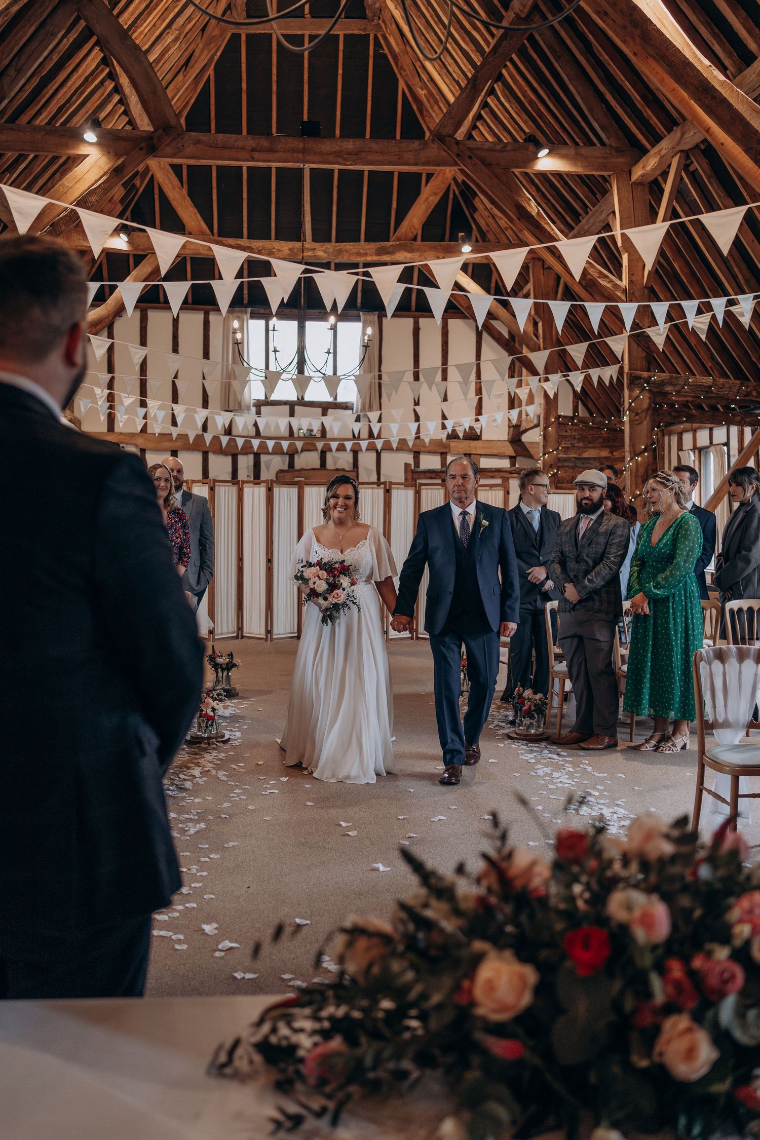 Wedding ceremony in a rustic barn venue with exposed wooden beams and romantic string lights overhead.