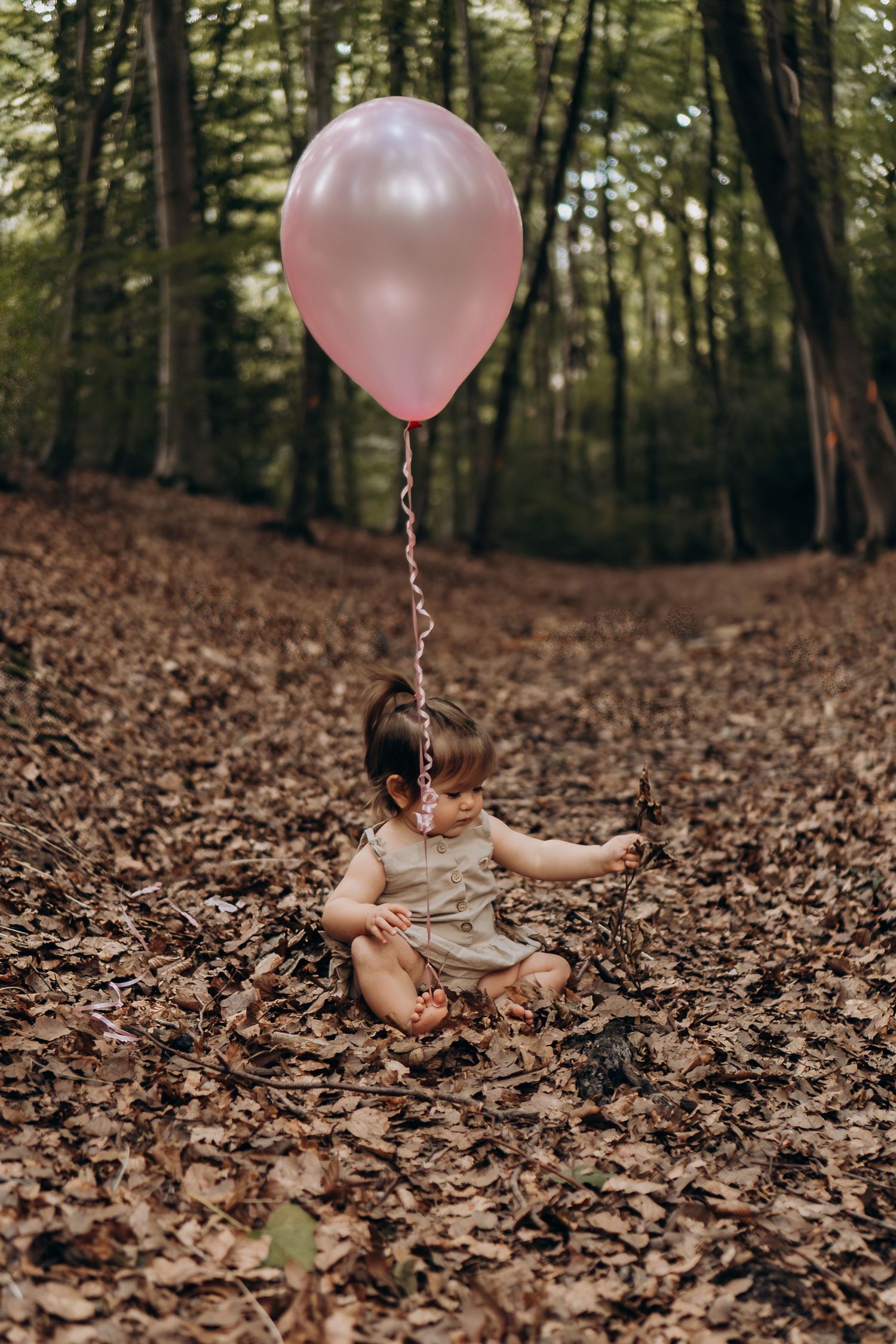 A pink balloon floats above fallen autumn leaves in a wooded forest setting.