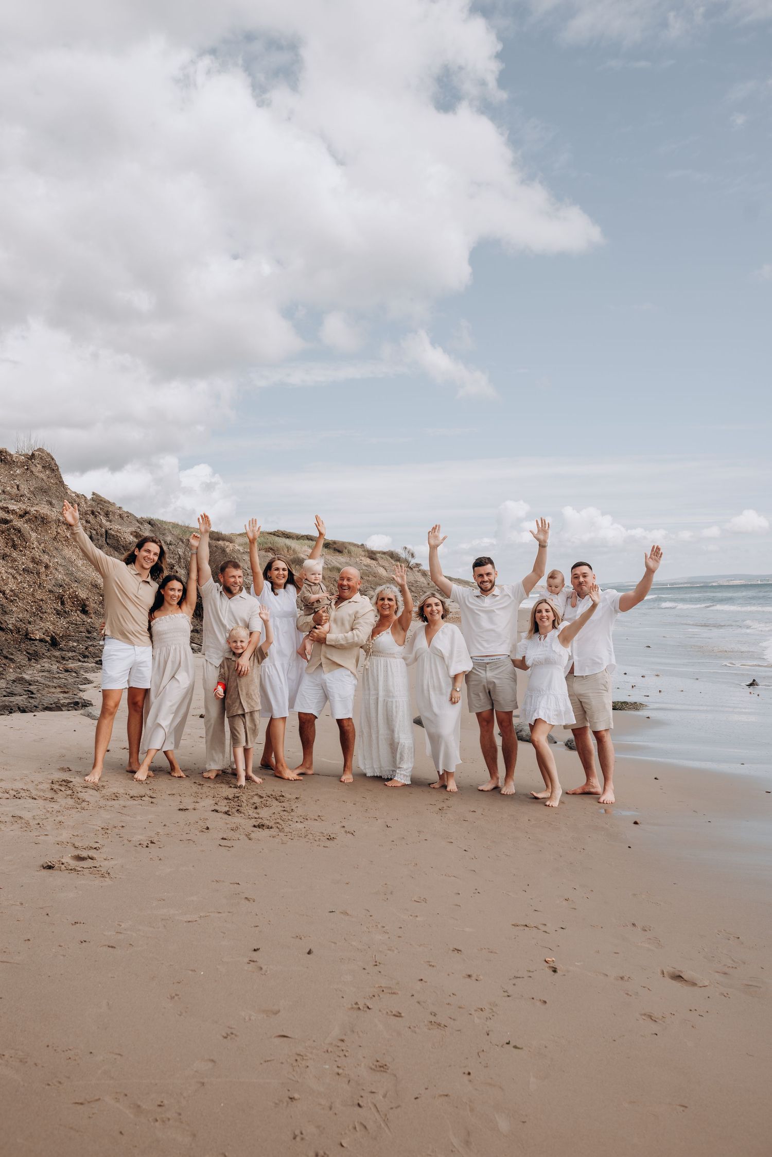 Group photo of people in white outfits celebrating on beach with ocean backdrop.