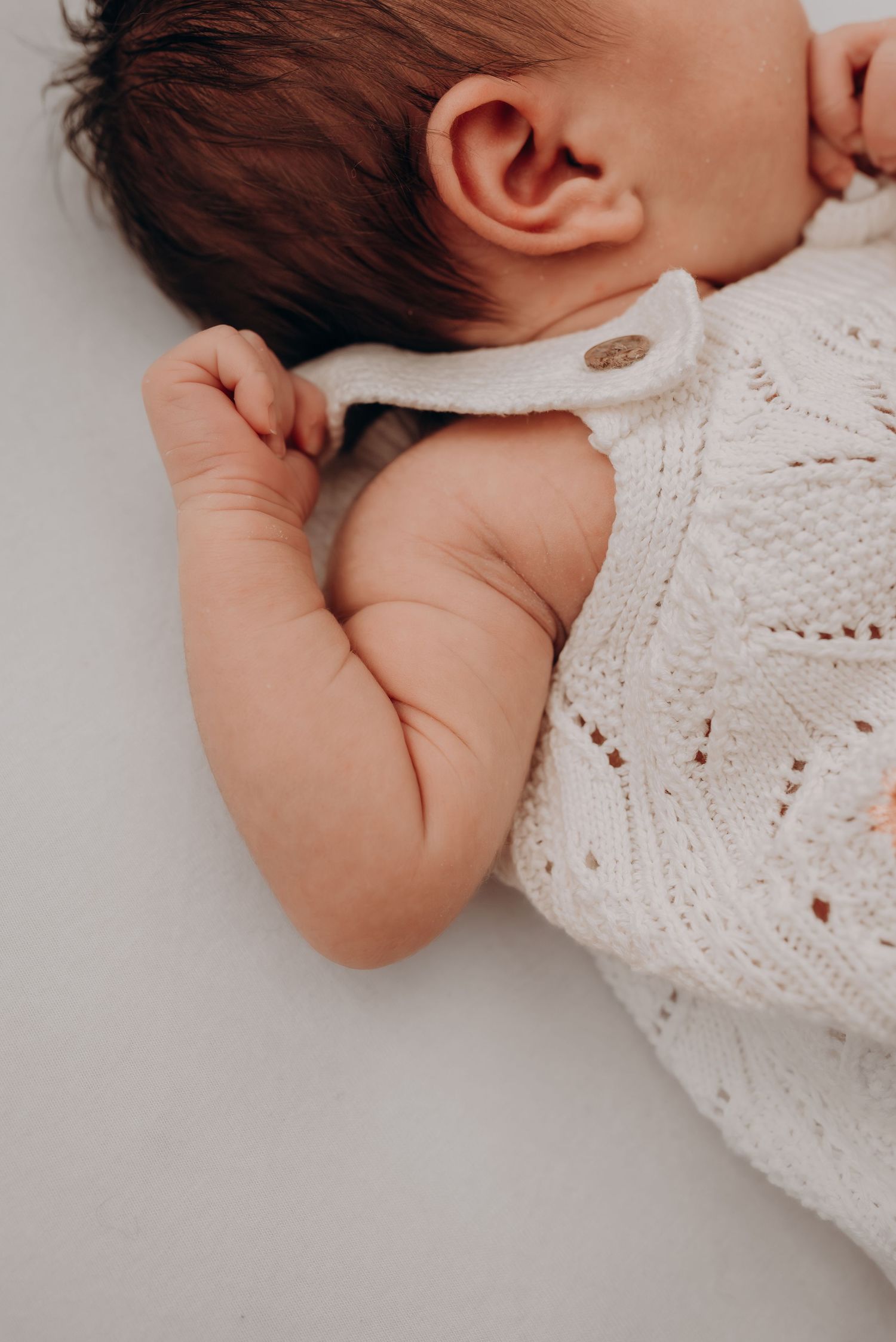 Close-up of an infant in a white knit sweater resting peacefully.