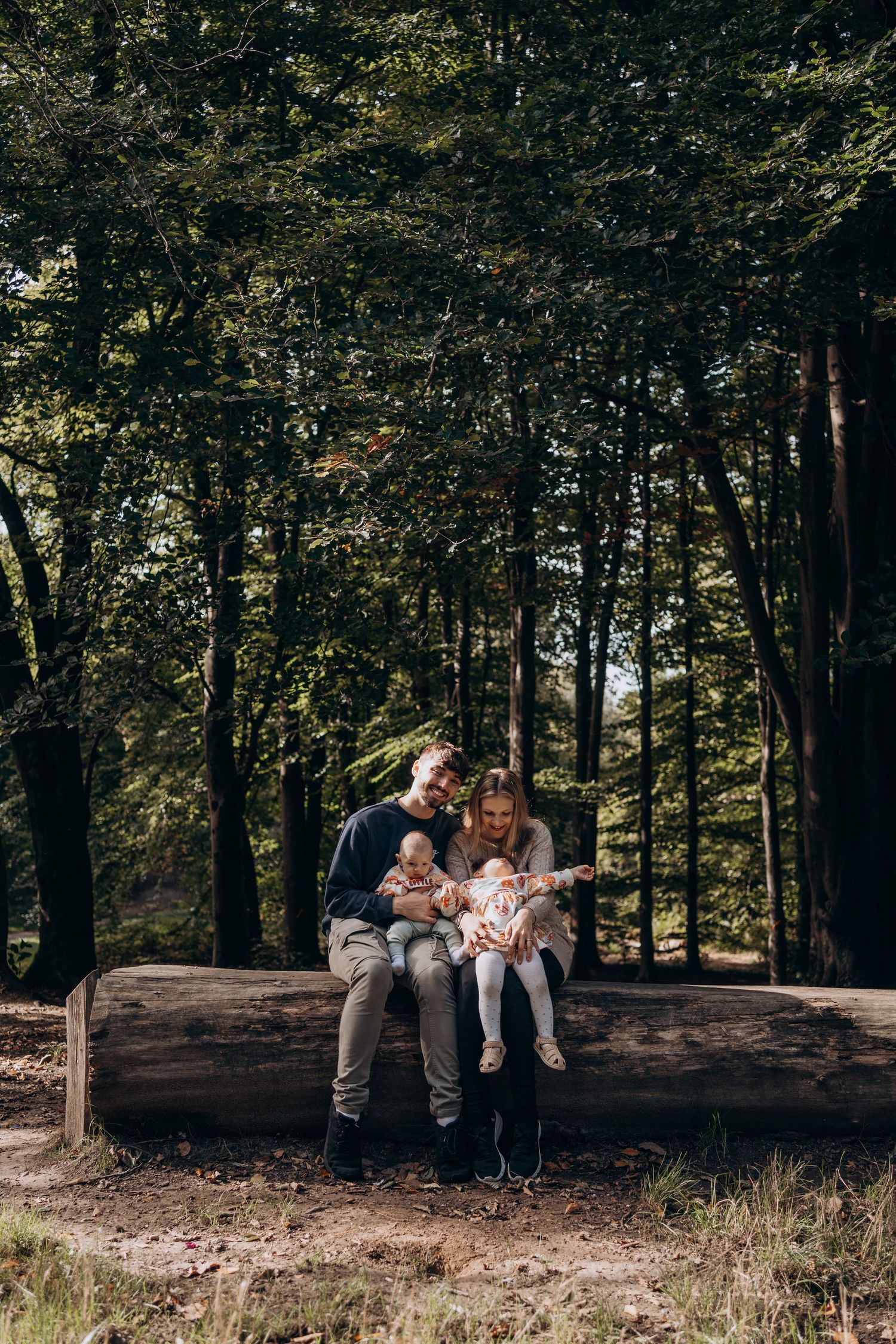 A family sits together on a fallen tree trunk in a wooded forest setting during an outdoor photo session.