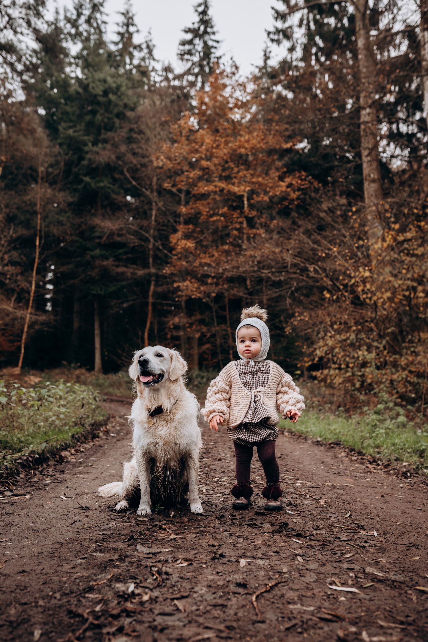Child and dog sitting together on a forest path during autumn.