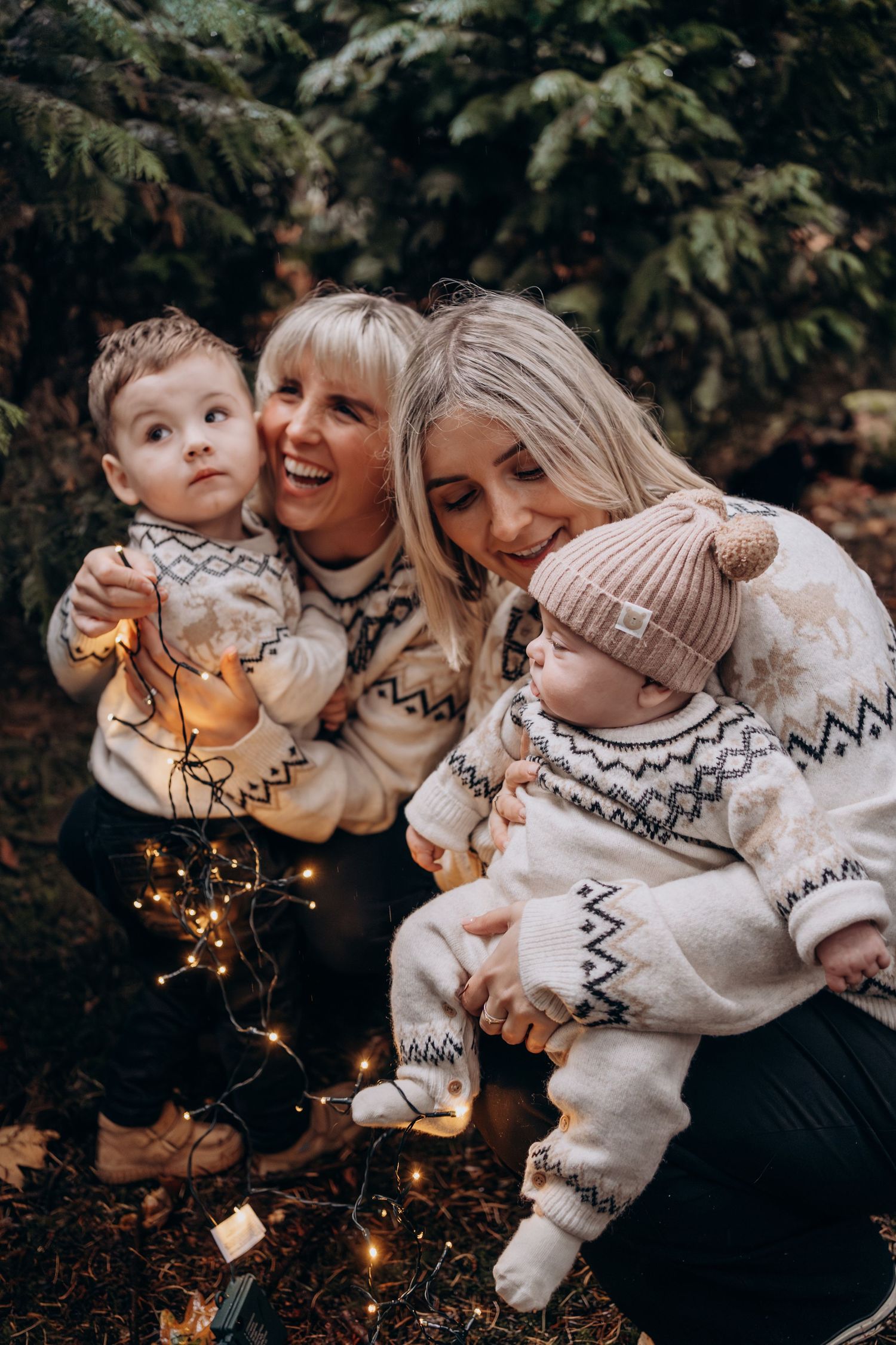 A family wearing matching white winter sweaters plays with sparklers together in a cozy outdoor photoshoot.
