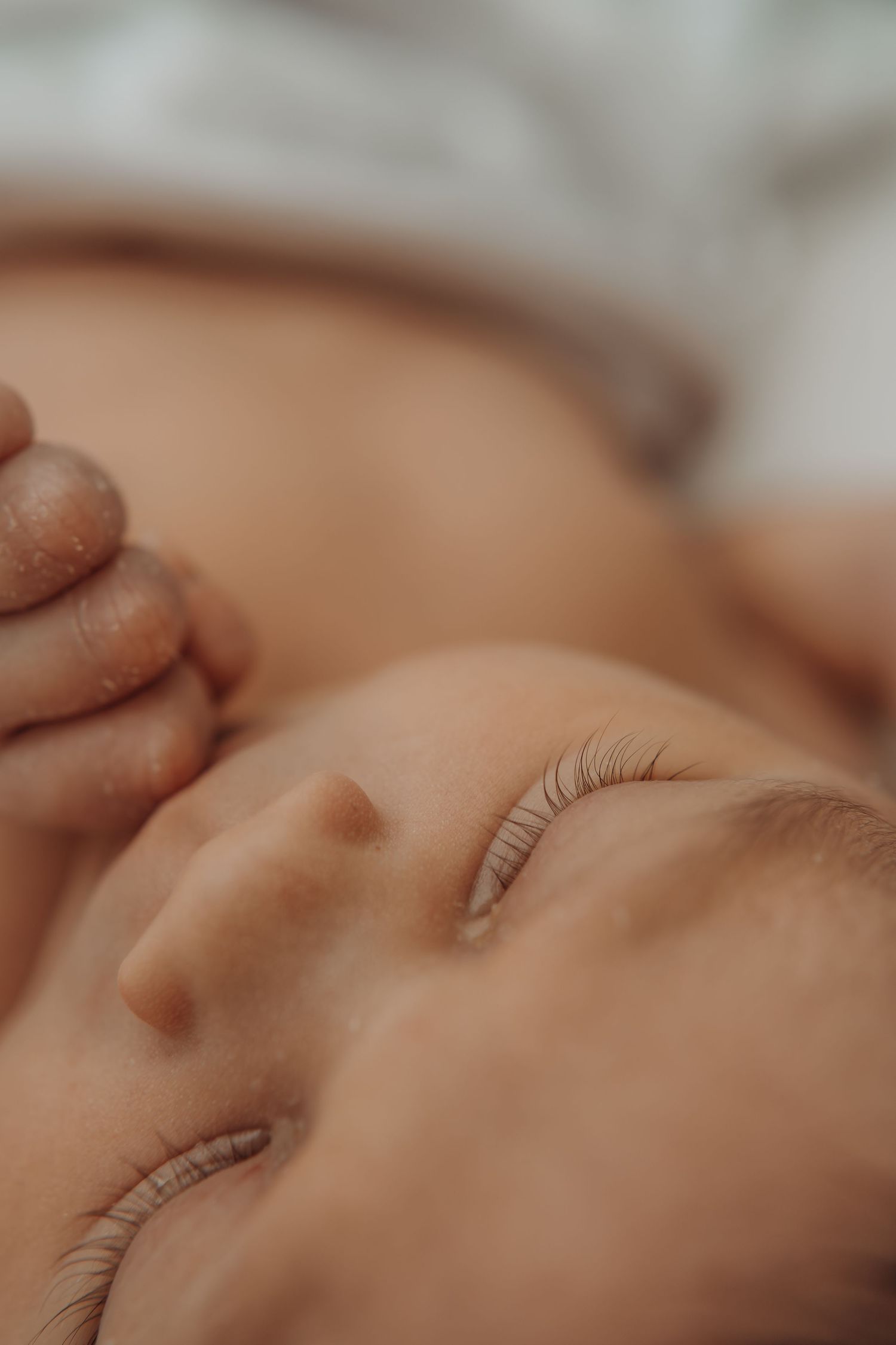Close-up of a peaceful sleeping newborn baby with tiny clenched fist and delicate eyelashes.