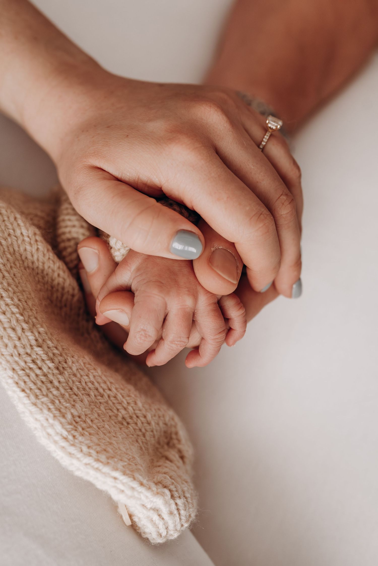 Close-up of hands gently touching newborn baby wrapped in knit blanket.