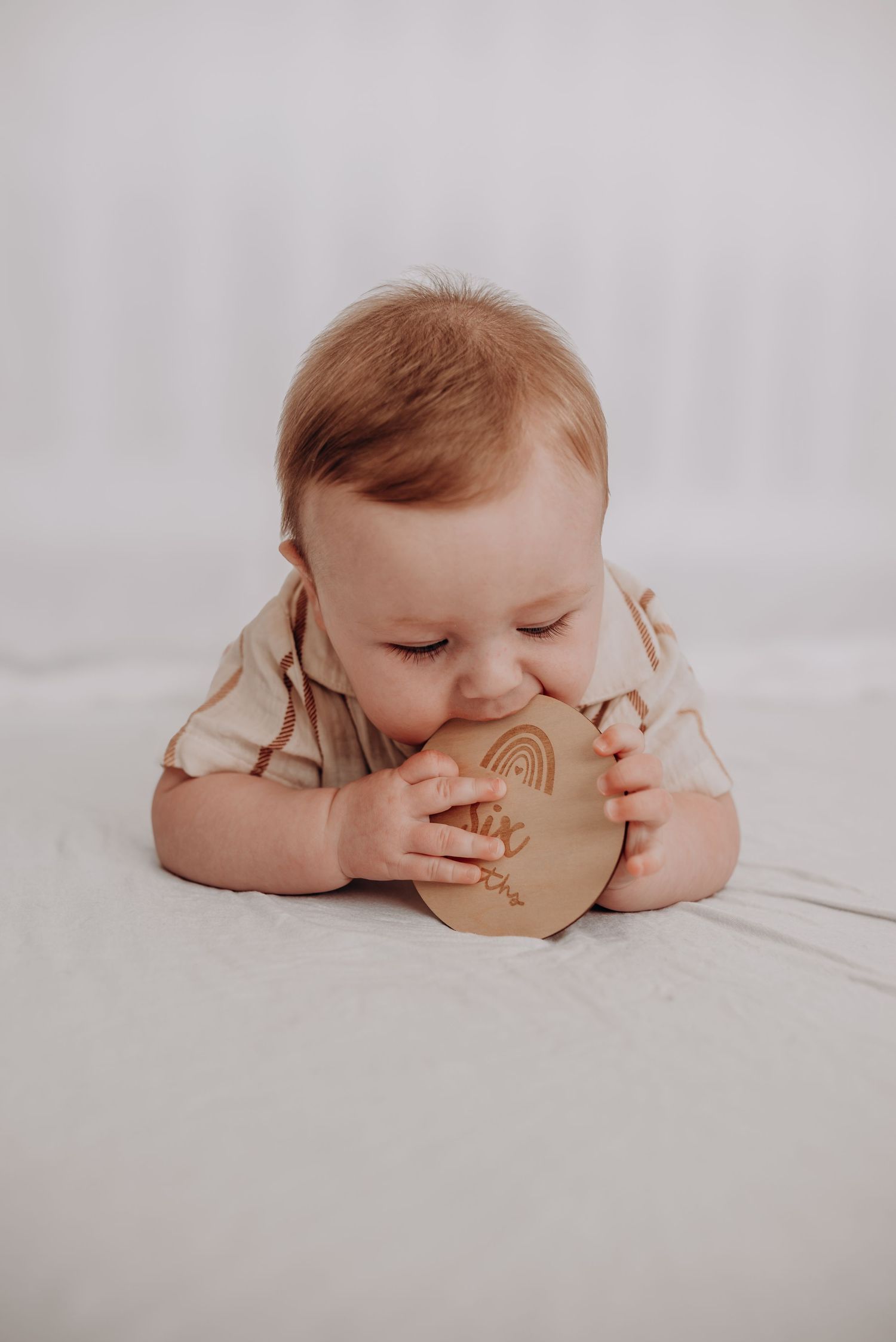 Baby lying on white surface examining a wooden toy with curiosity.