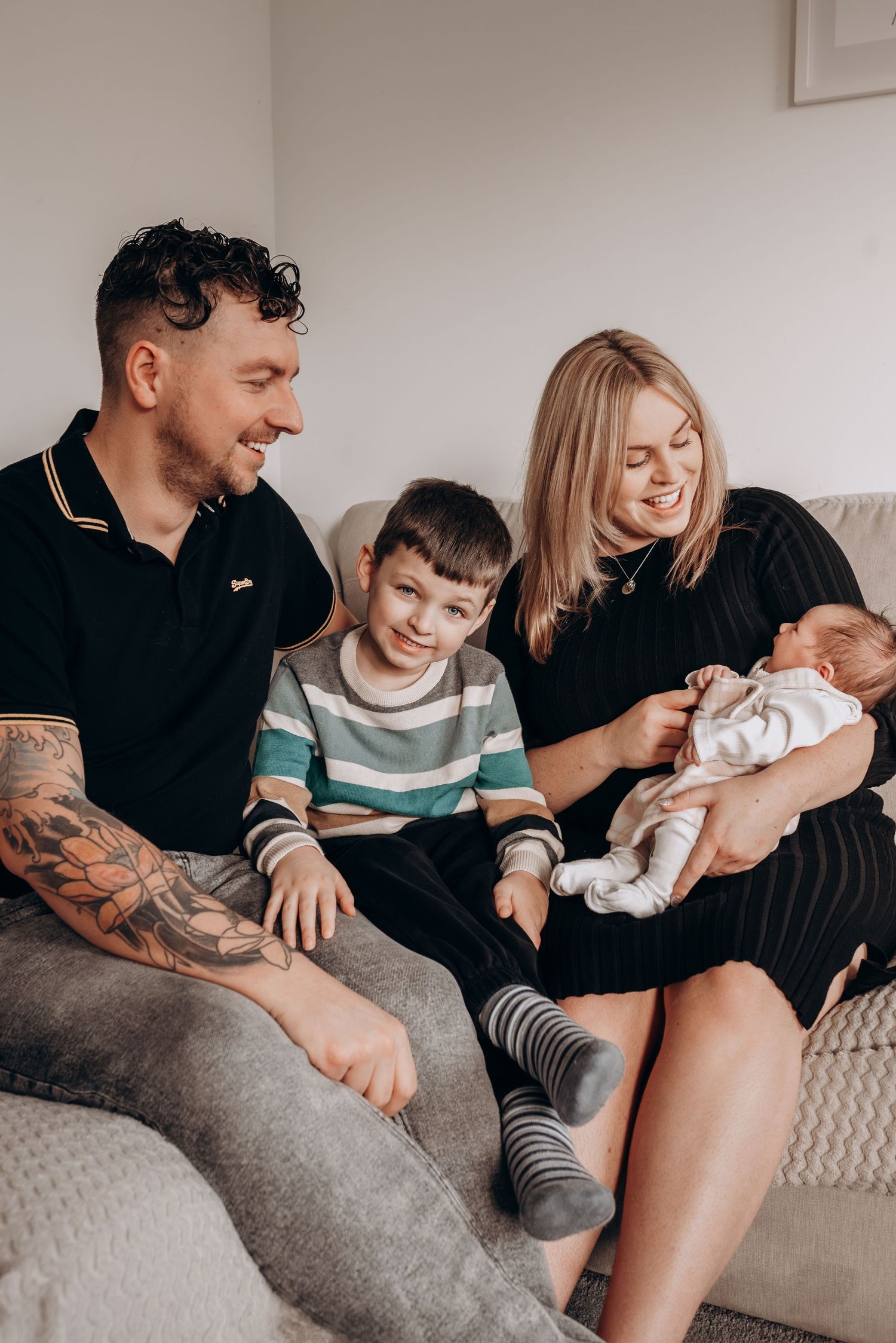 Family relaxing together on grey couch, sharing joyful moments with their newborn baby.