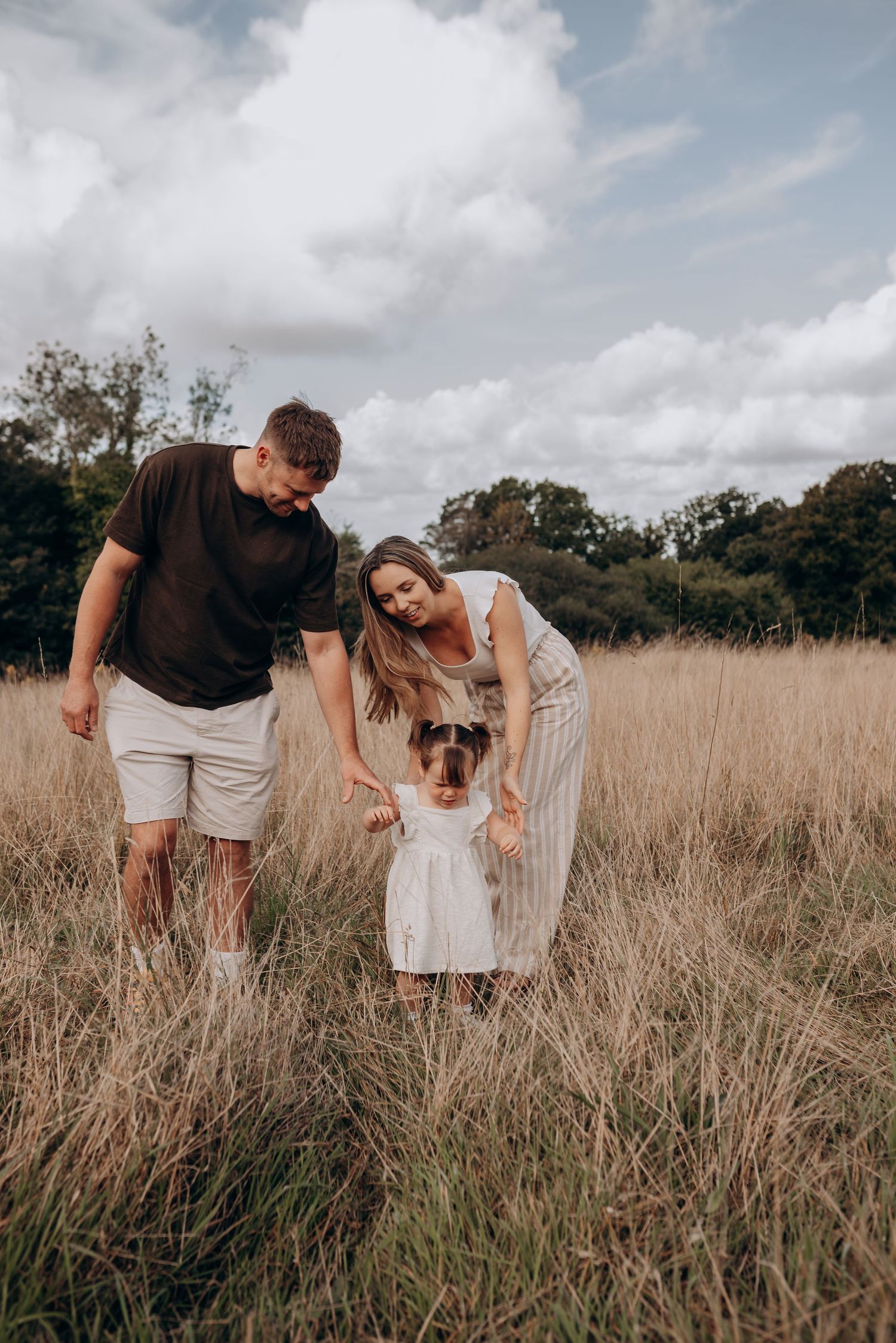 A family walks together through tall grass in a field during golden hour.