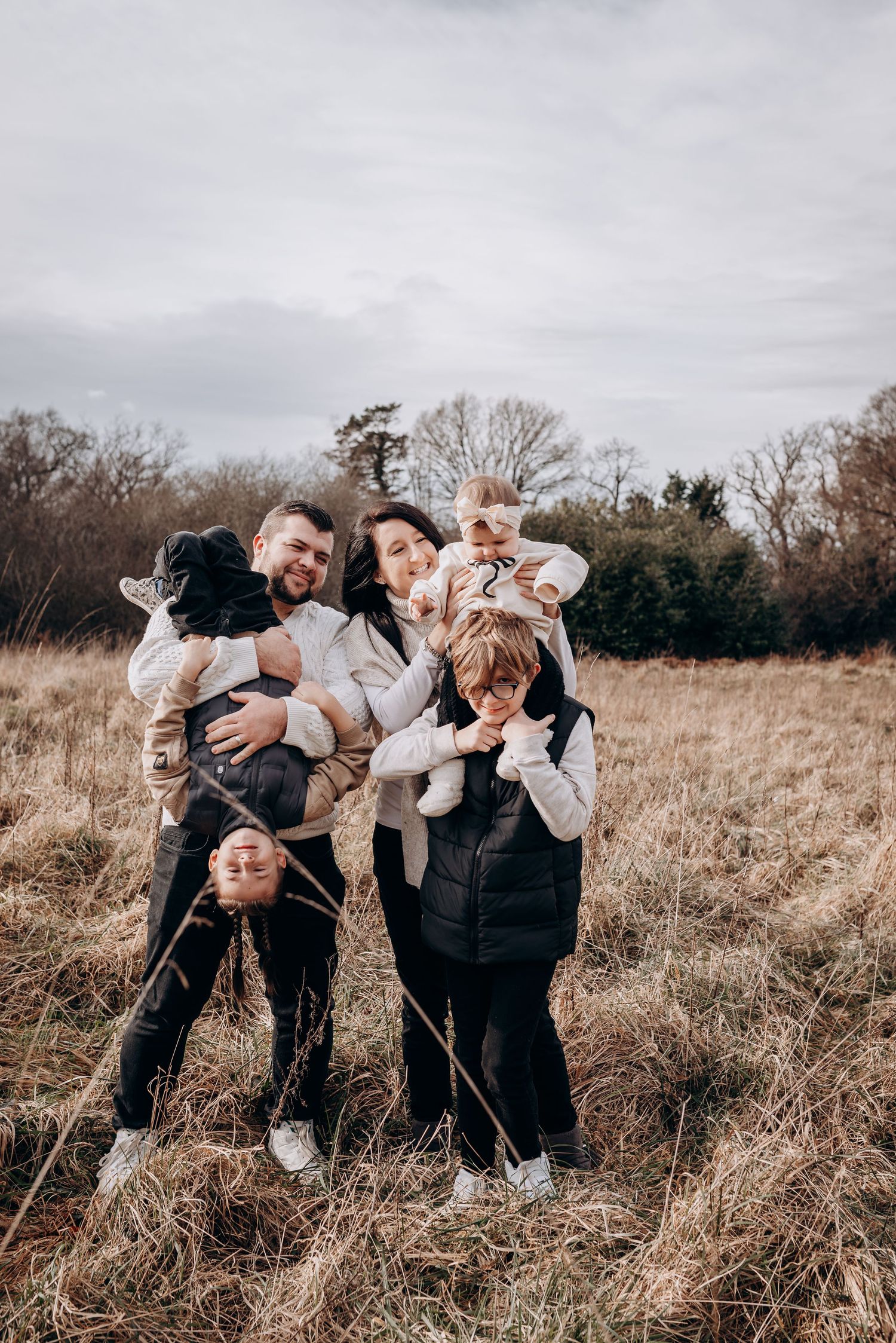 Family group posing playfully in tall grass field on cloudy day.