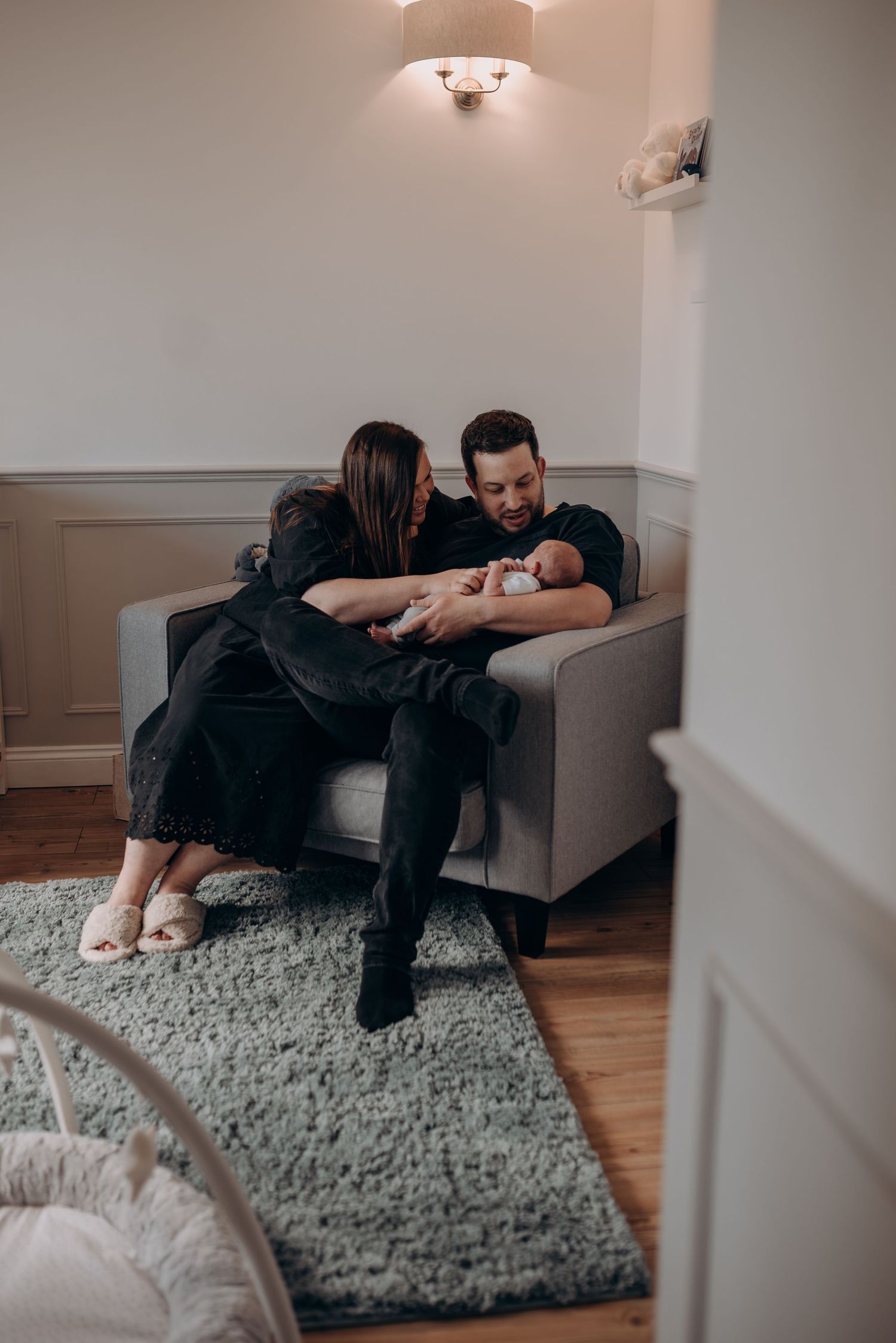 Intimate family moment with newborn on a gray armchair in modern living room.