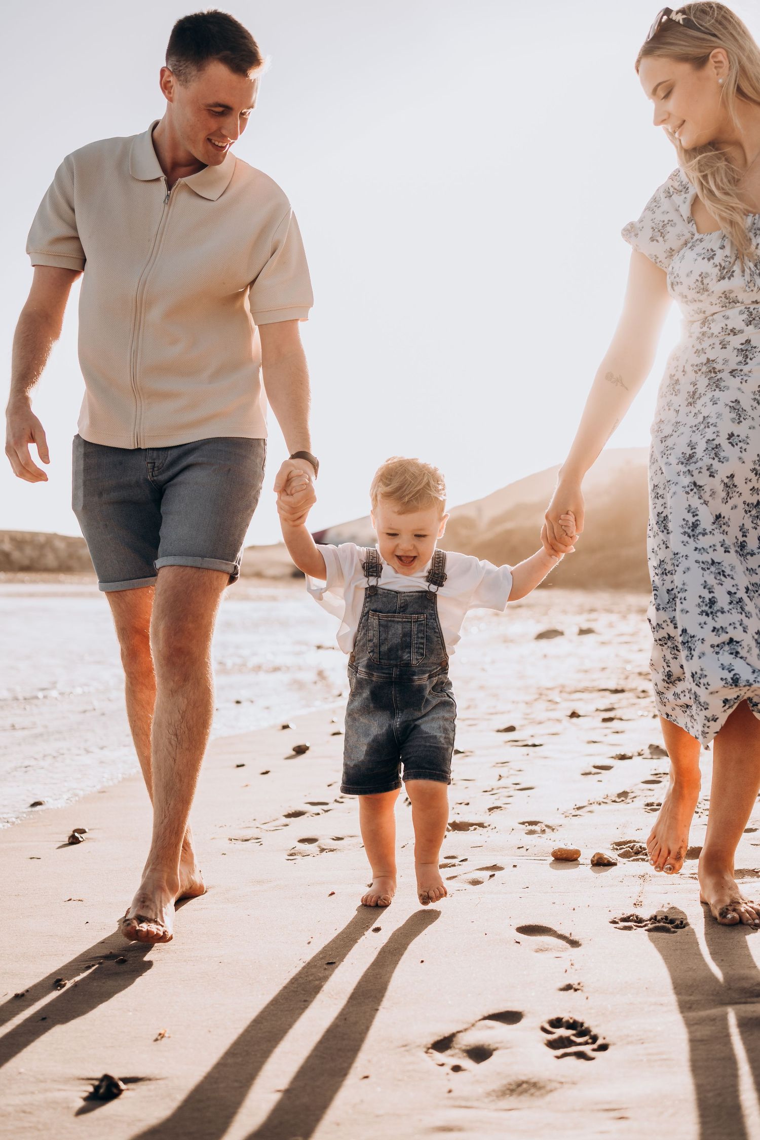 Family walking together on a sunny beach leaving footprints in the sand.