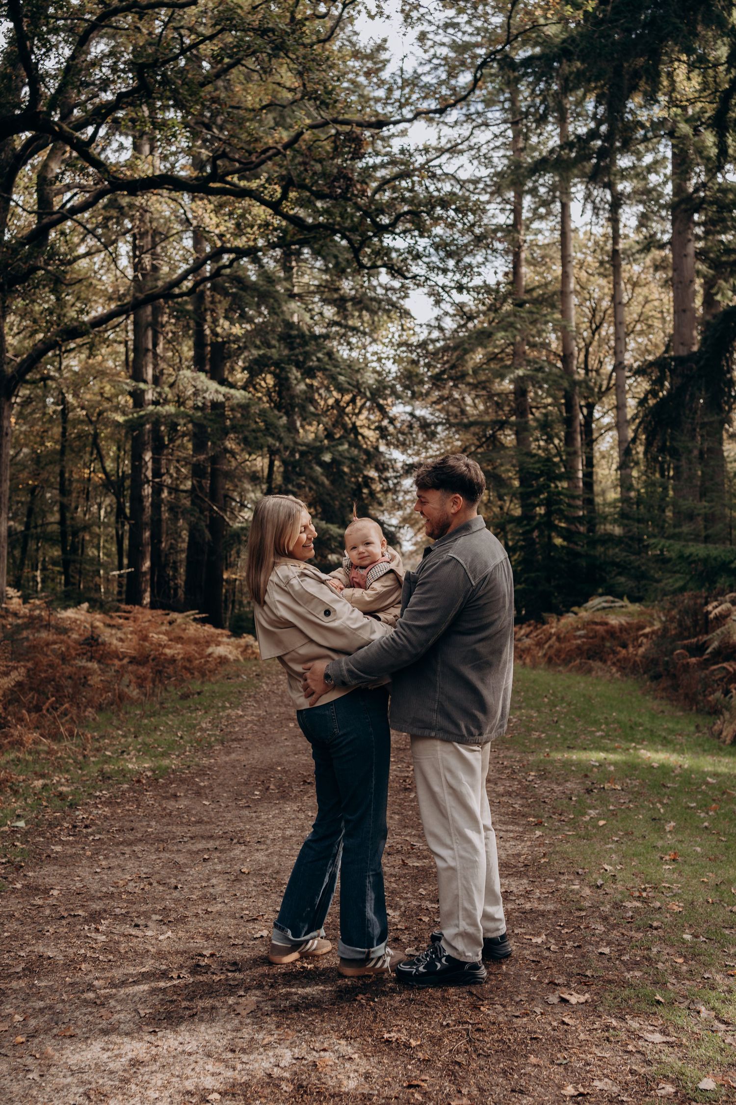 A couple embraces while dancing together on a forest path surrounded by tall trees during an autumn day.
