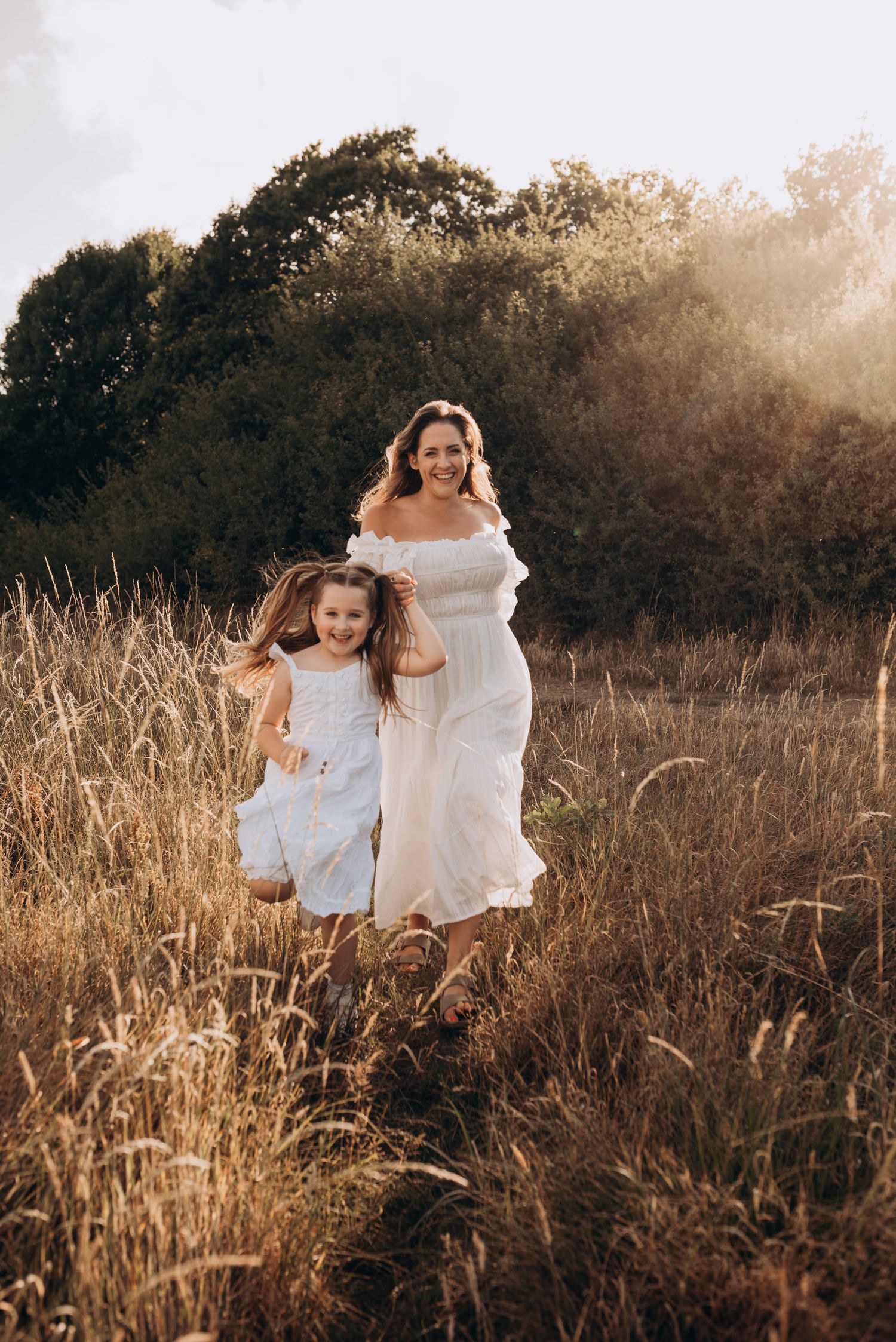 A pair in white dresses dance and twirl together in a sunlit golden field at sunset.