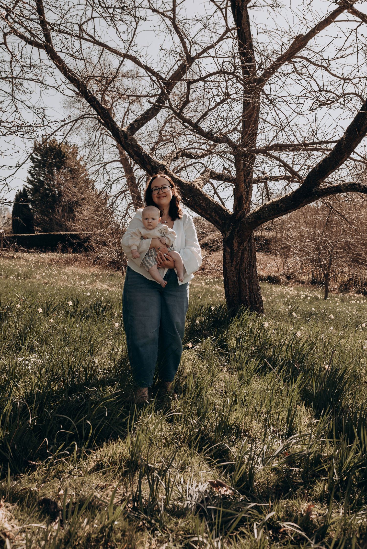 Spring outdoor photoshoot under blooming trees in sunlit meadow.