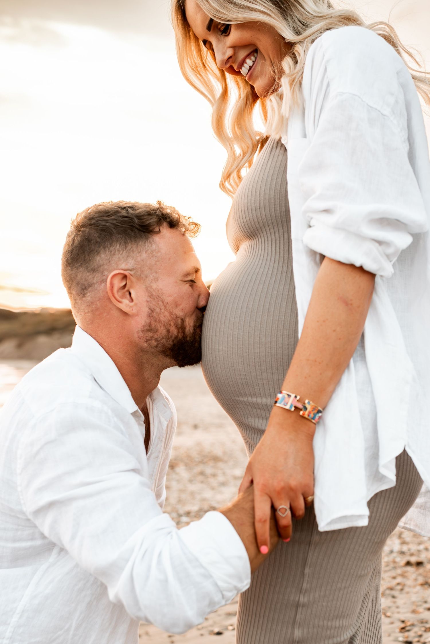 An intimate maternity moment captured on the beach during golden hour.