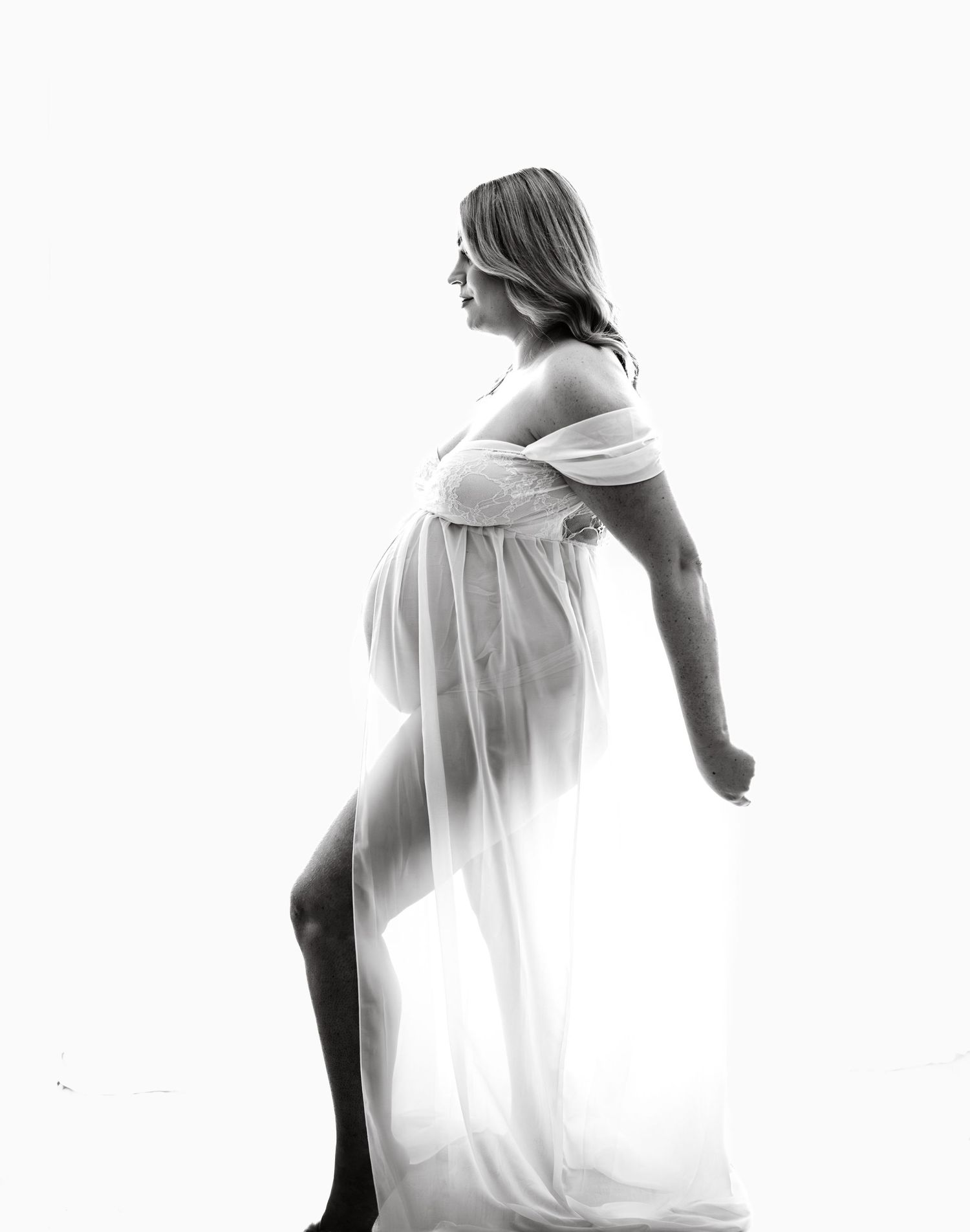 Artistic maternity silhouettes in white dress against bright background.