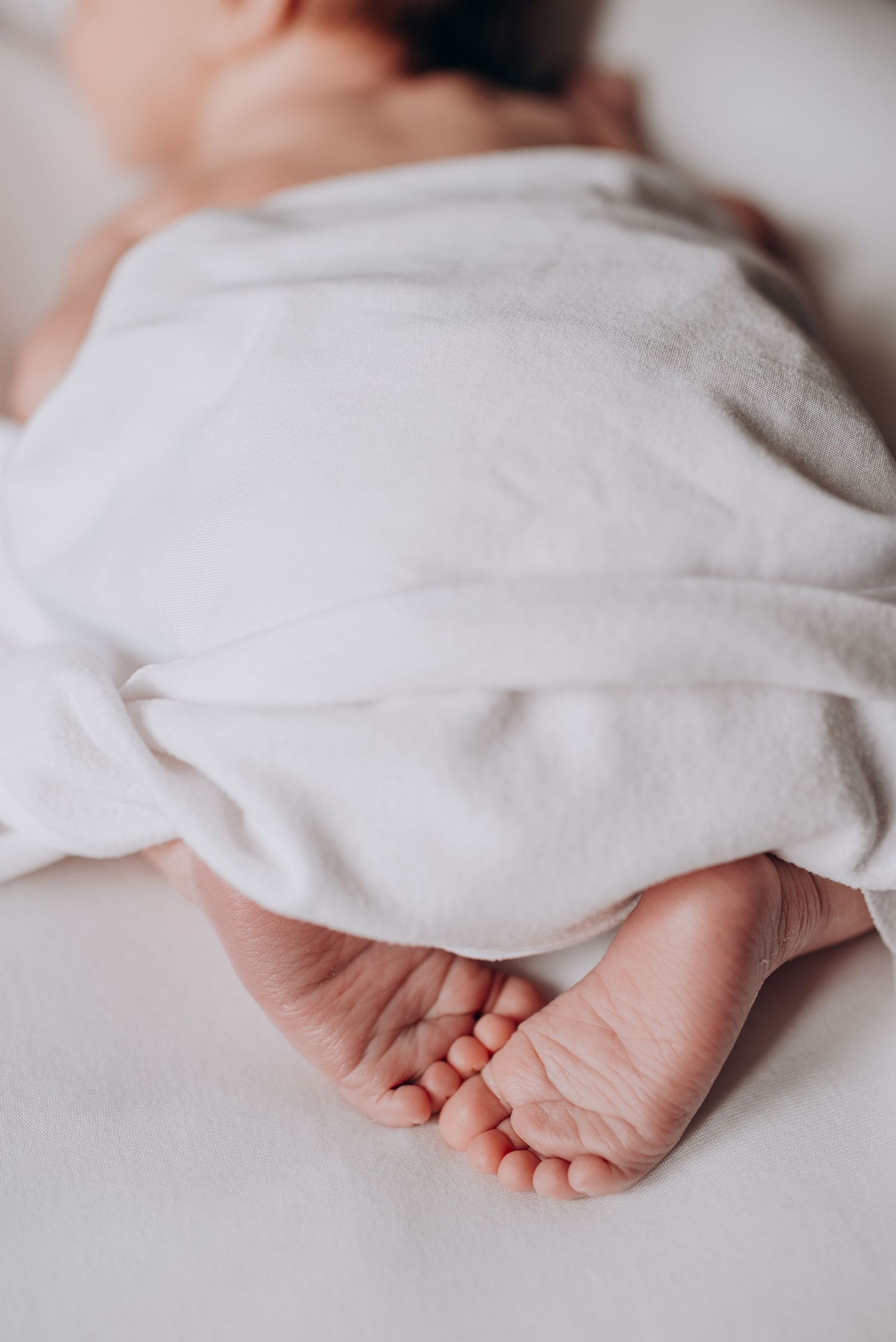 Delicate newborn baby feet peeking out from beneath a white blanket.