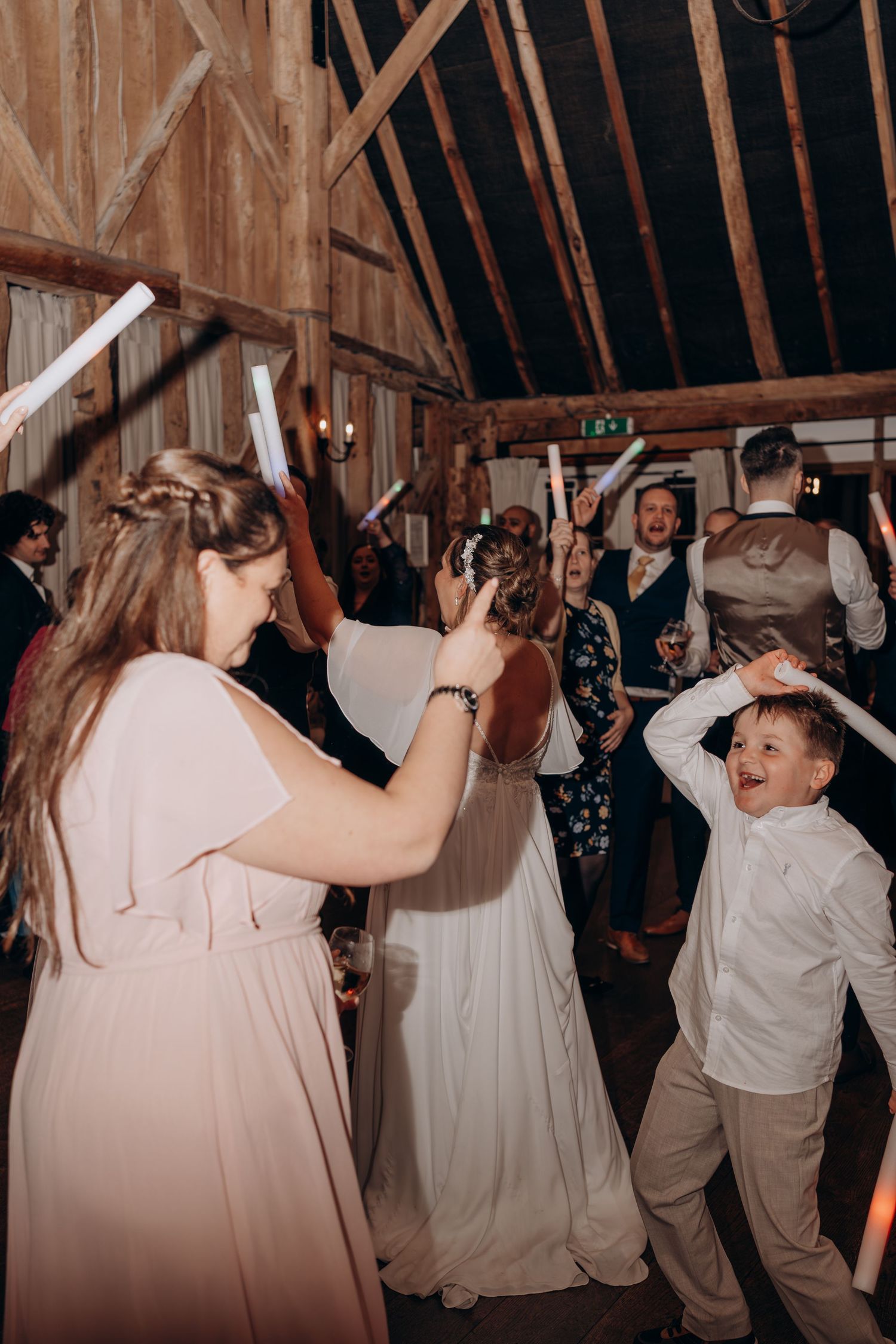 Wedding reception guests dancing and celebrating inside a rustic wooden barn venue with exposed beams and warm lighting.