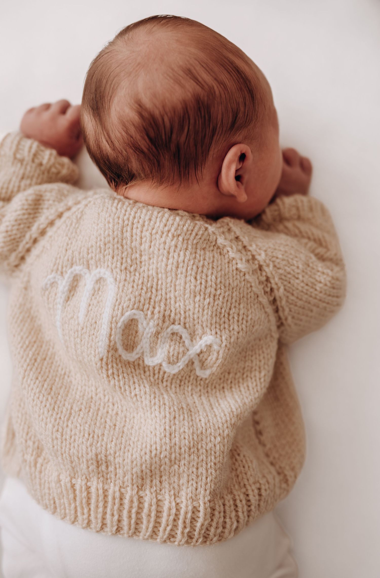 Newborn baby wearing soft beige knit sweater with text.