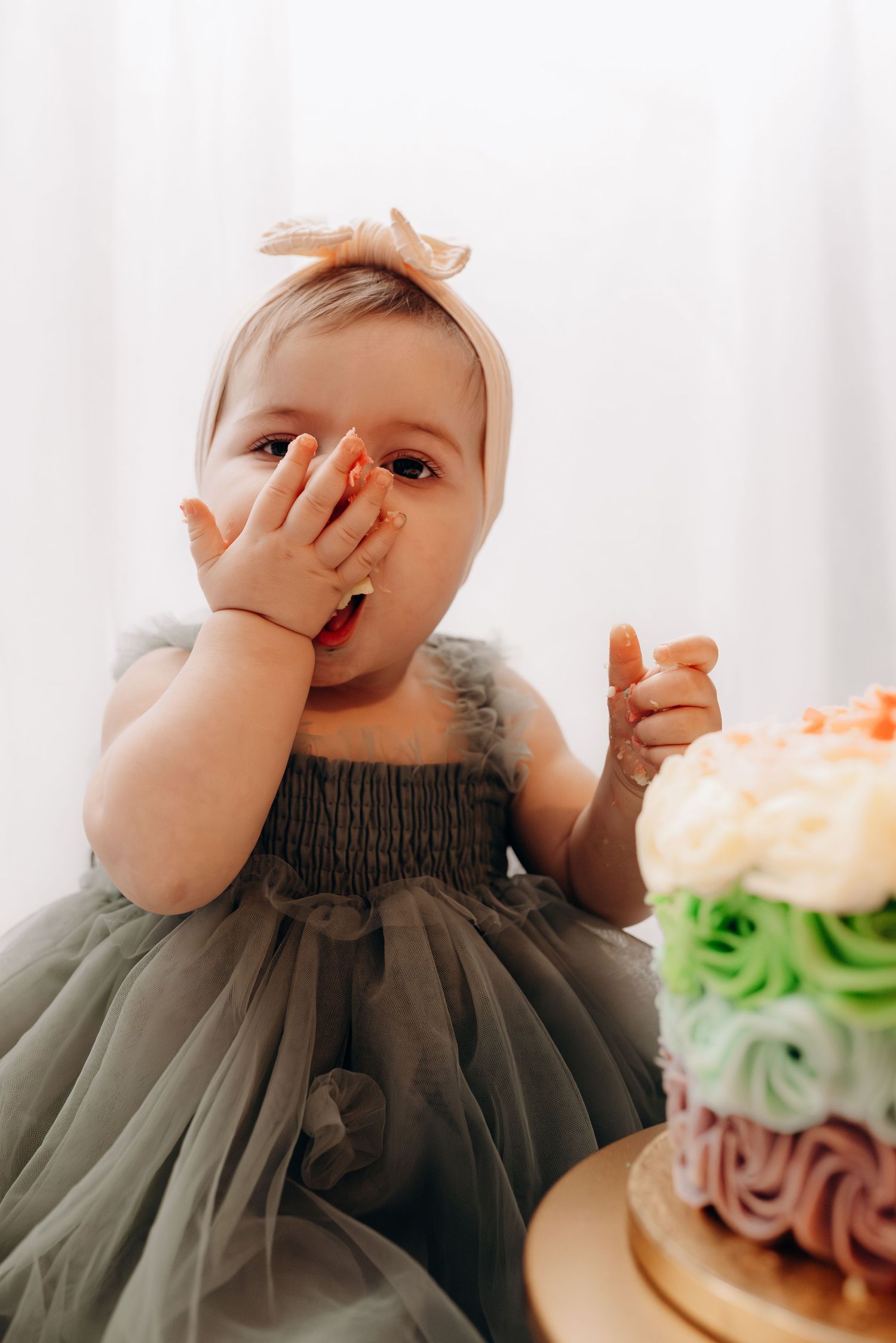 Baby wearing dark tulle dress reaching for colorful birthday cake during cake smash session.