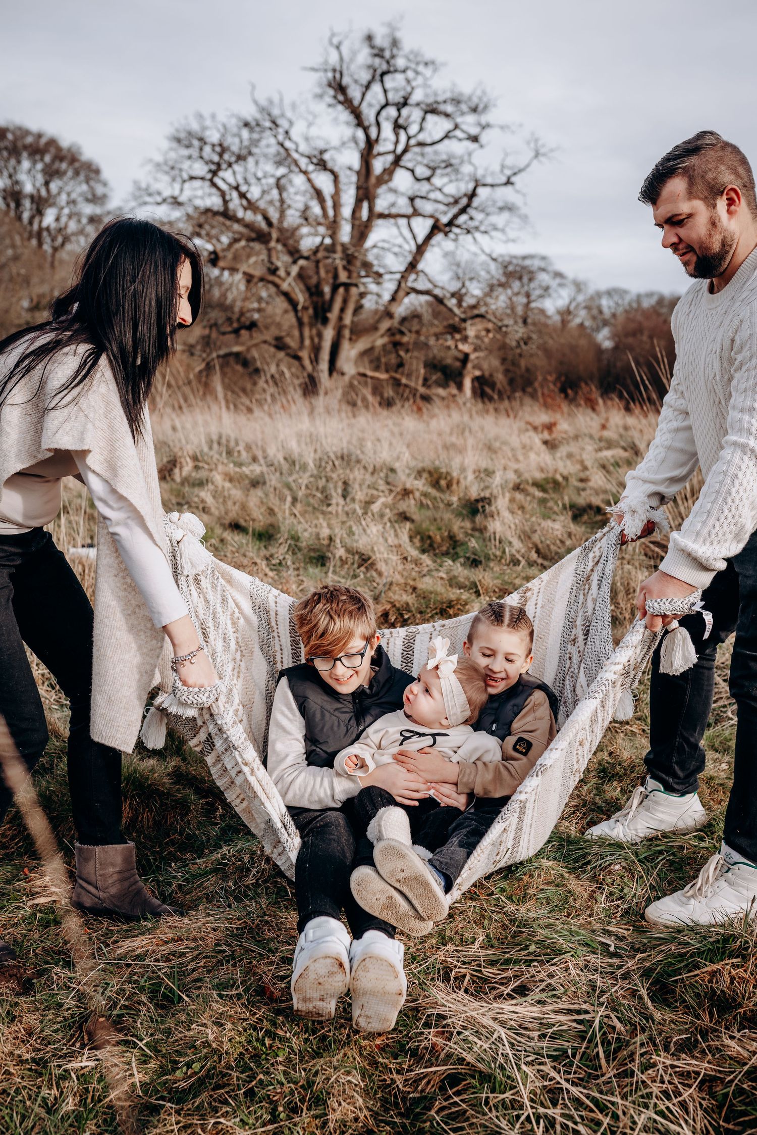 Family playing together in a grassy field wearing coordinated white and neutral outfits.
