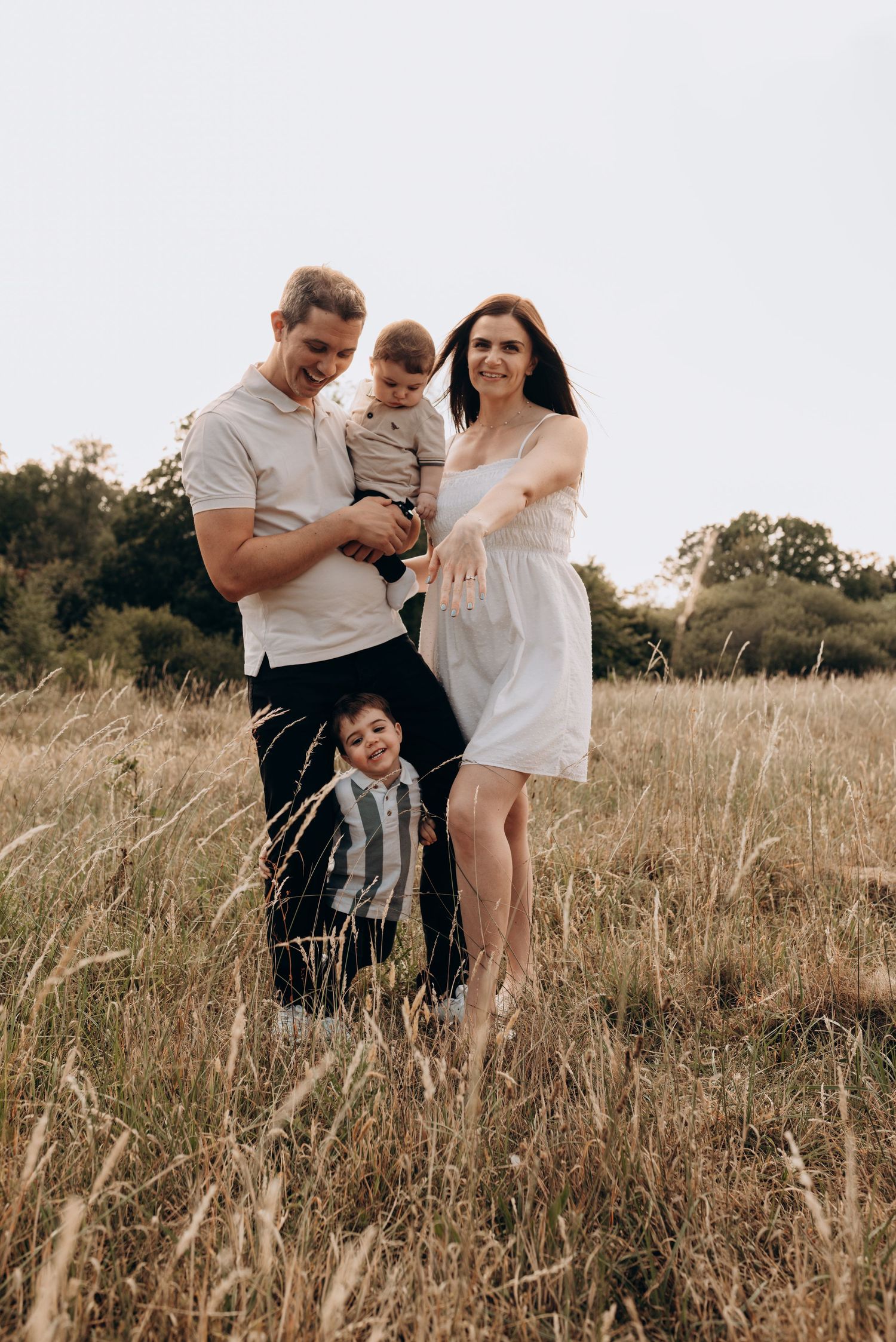 A family shares a candid moment together in a sunlit meadow with tall grass.