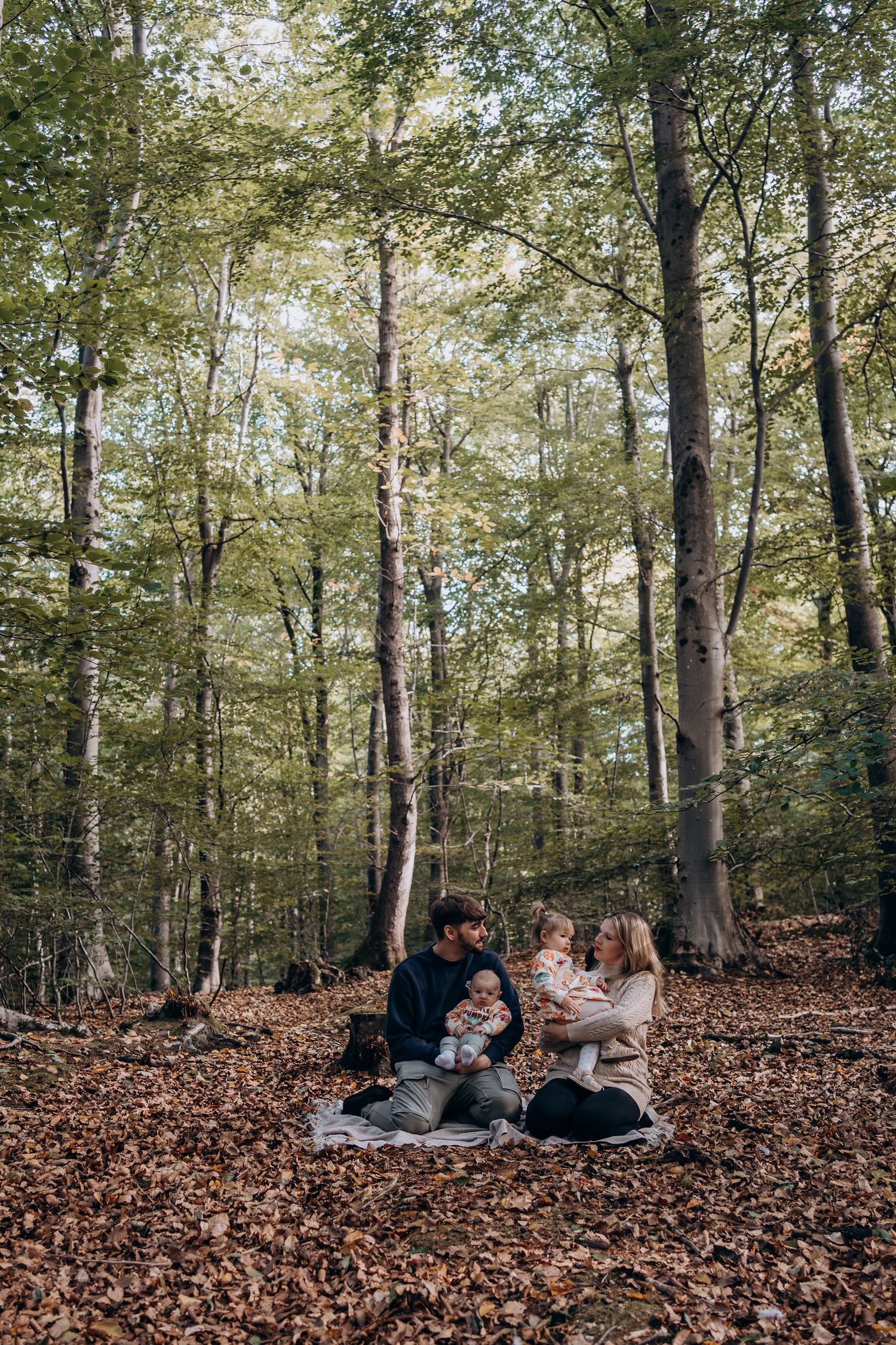 Family gathering on fallen autumn leaves in sunlit forest.