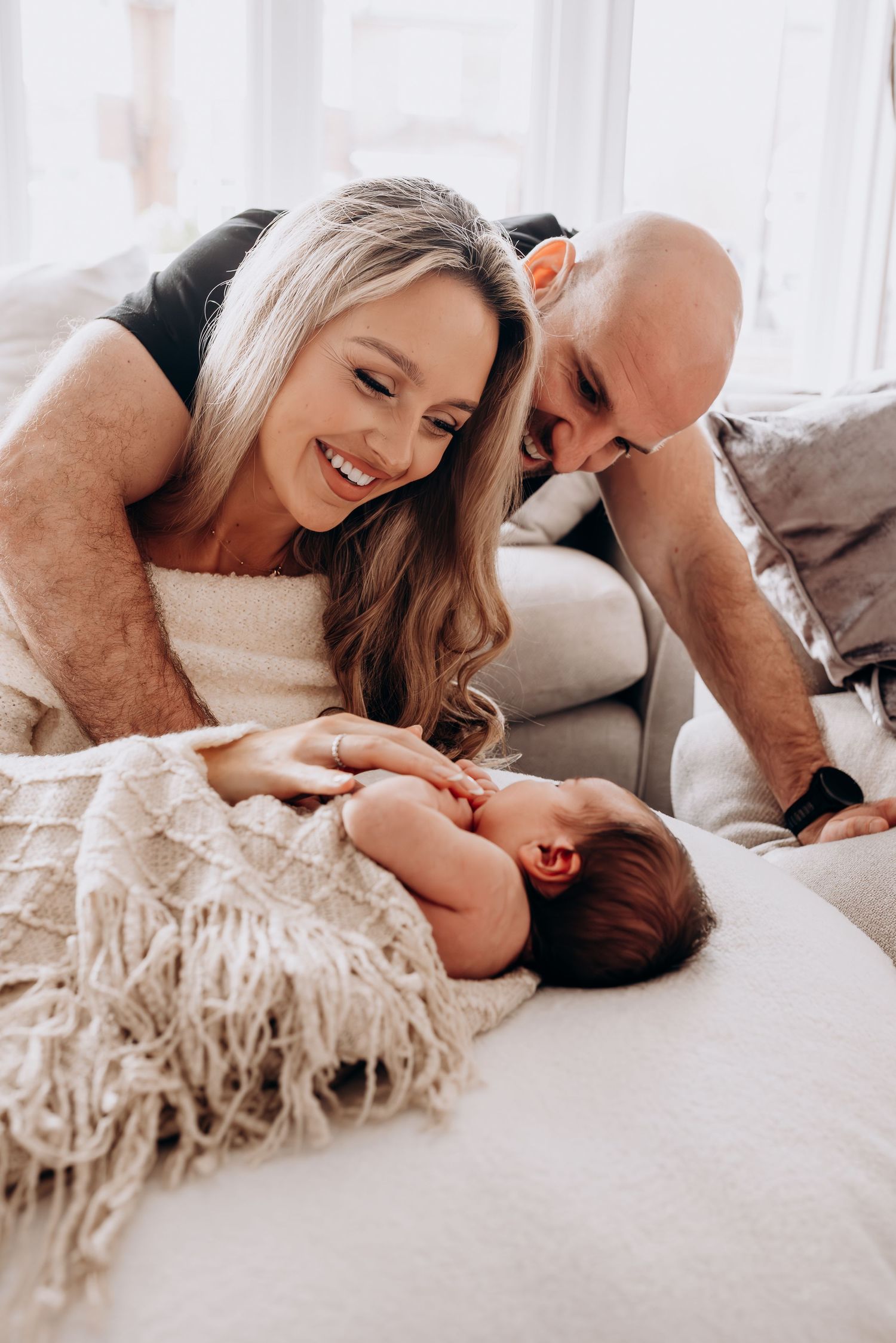 Parents sharing intimate moments with their newborn baby on white bedding.